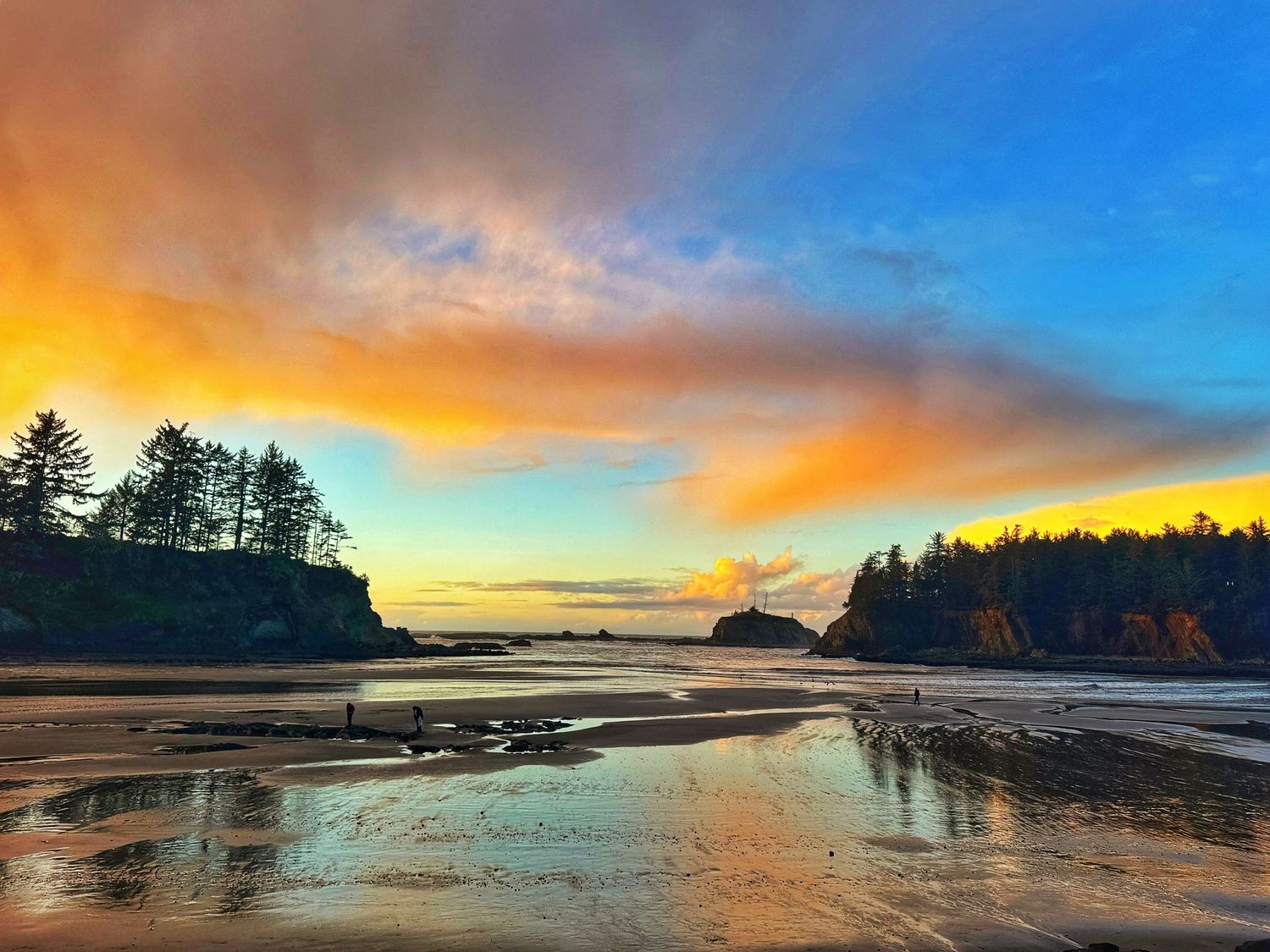 Vibrant sunset illuminates a coastal beach landscape with dramatic orange and blue sky reflections.