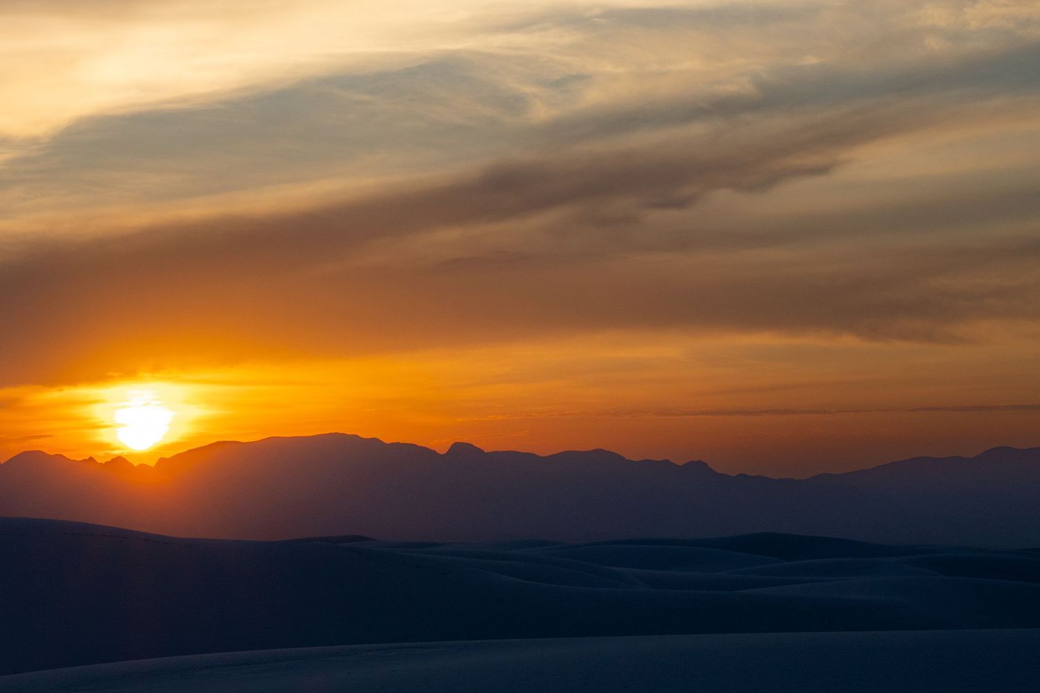 A panoramic sequence of sunset photos showing the sun descending behind mountain silhouettes with dramatic orange clouds.