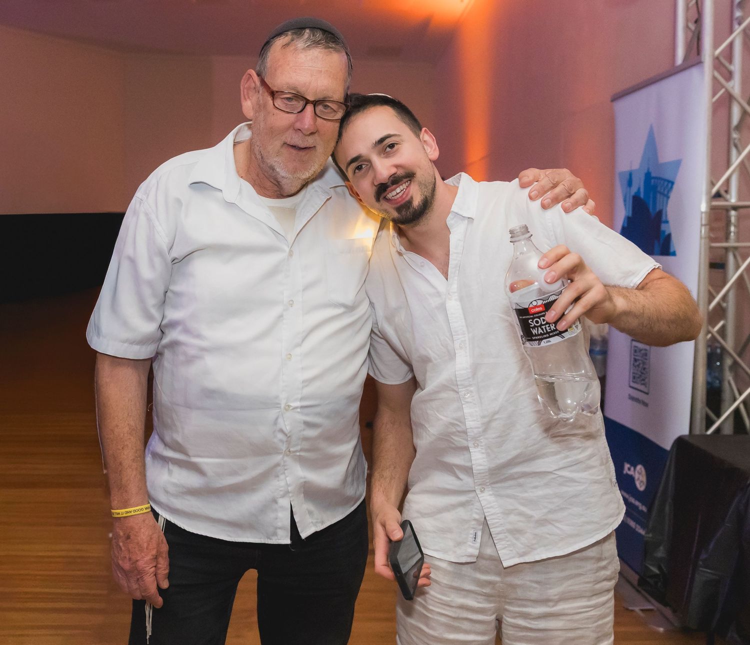 Two people in white shirts dancing and having fun at an event with orange lighting in the background.