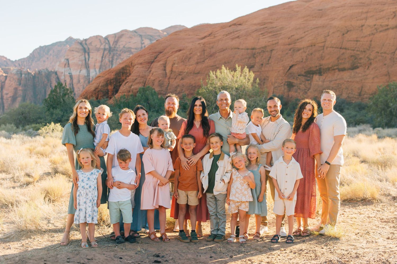 A group in coordinated earth-tone outfits poses together against scenic red rock formations in the desert landscape.