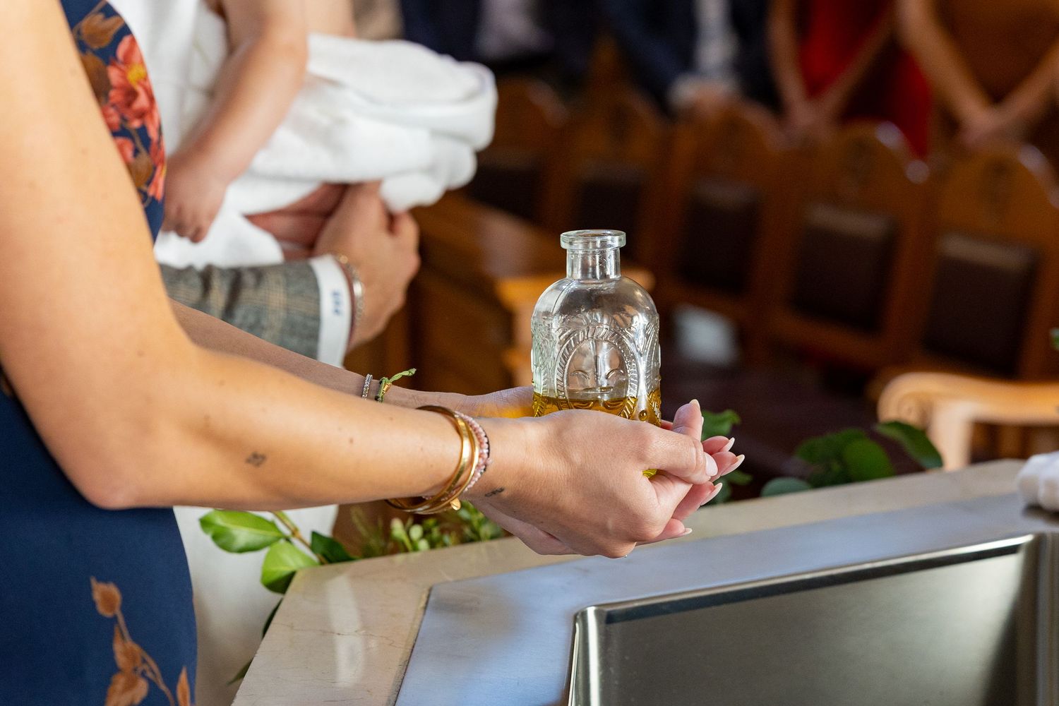 Detail photo of godmother holding oil during a child's baptism in Weston, MA.