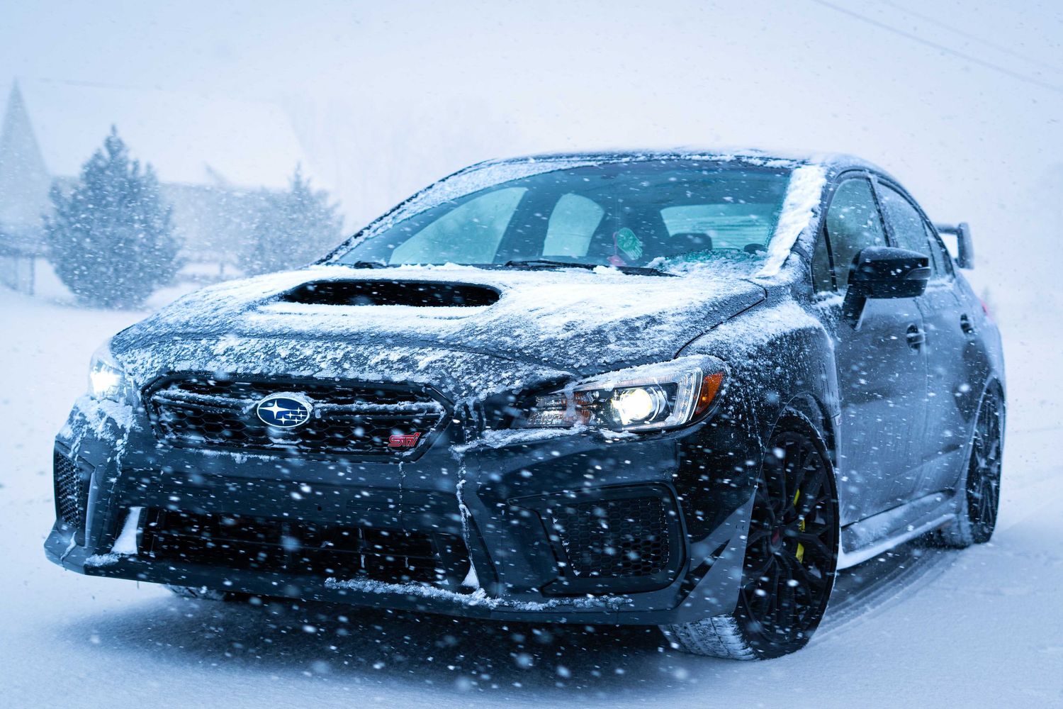 Black sports car drifting through snowy conditions on a winter track with falling snow creating dramatic action shots.