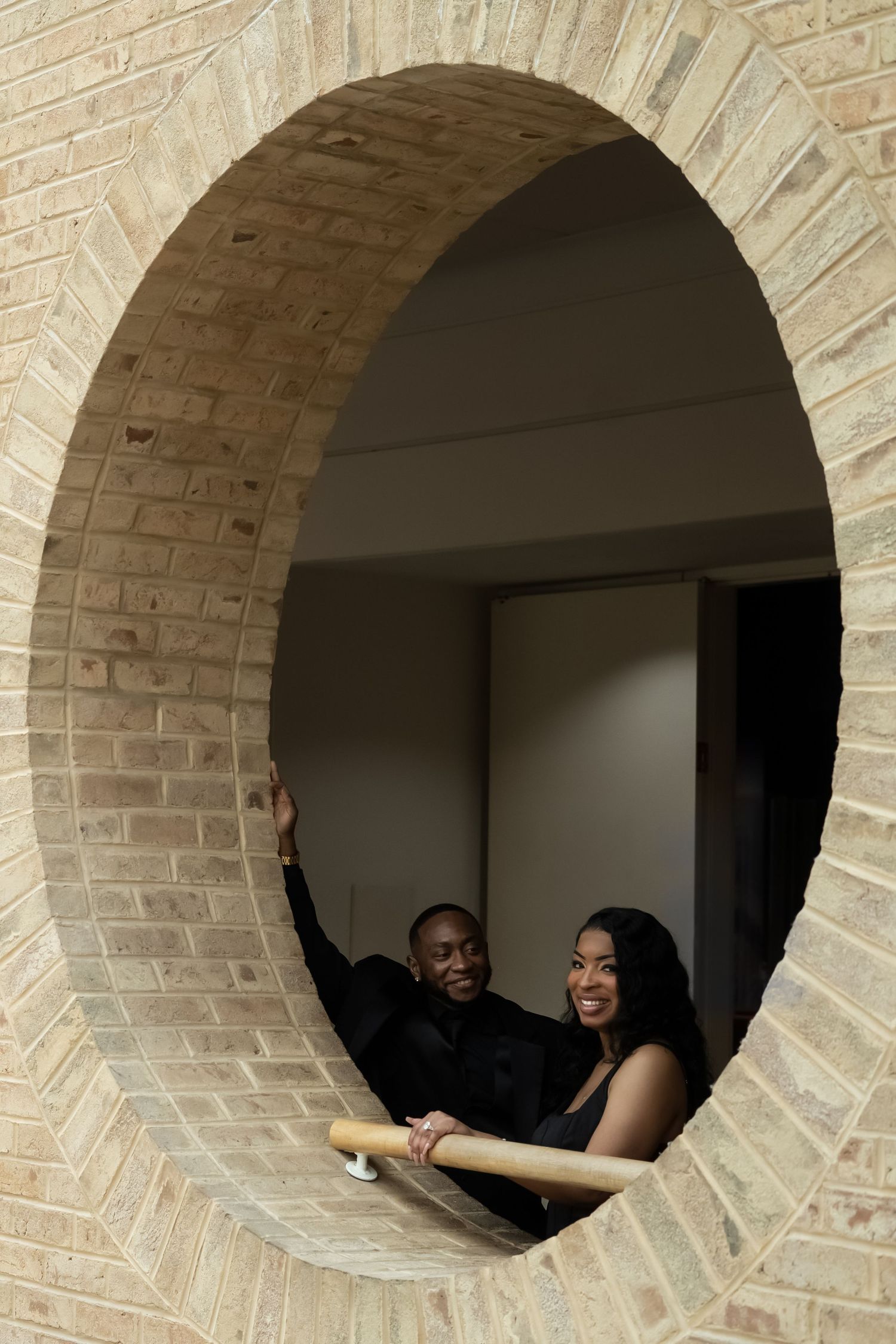 A couple walks hand in hand in front of a grand archway building with classical architecture under blue skies.
