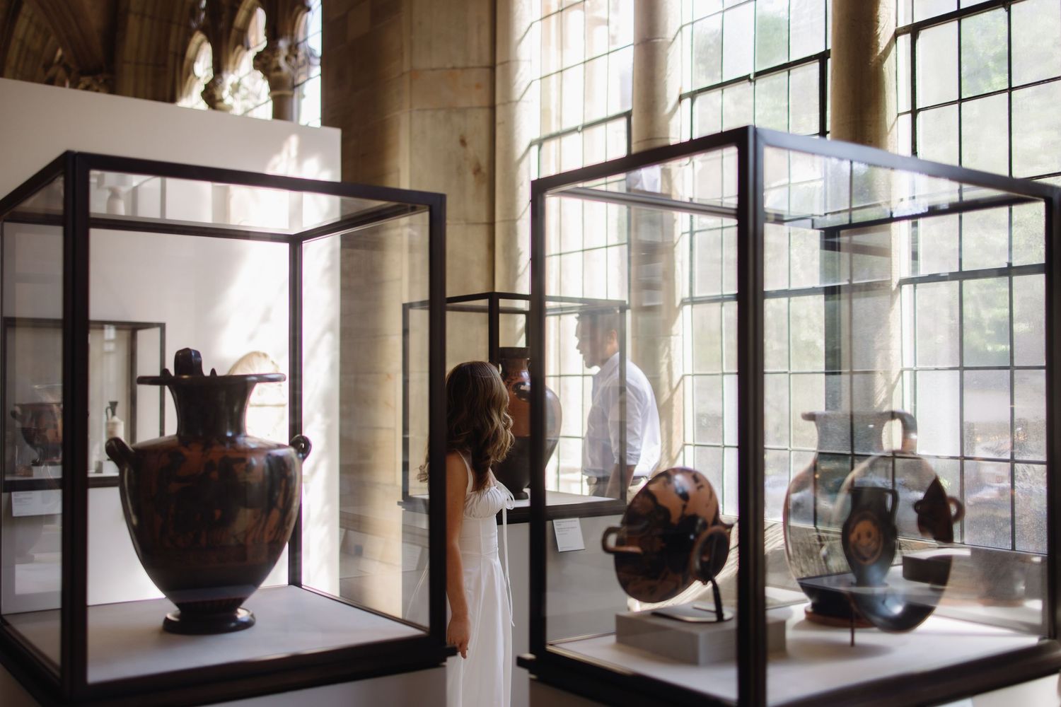 A series of display cases in a museum gallery showcasing ancient pottery and artifacts with natural light from windows.