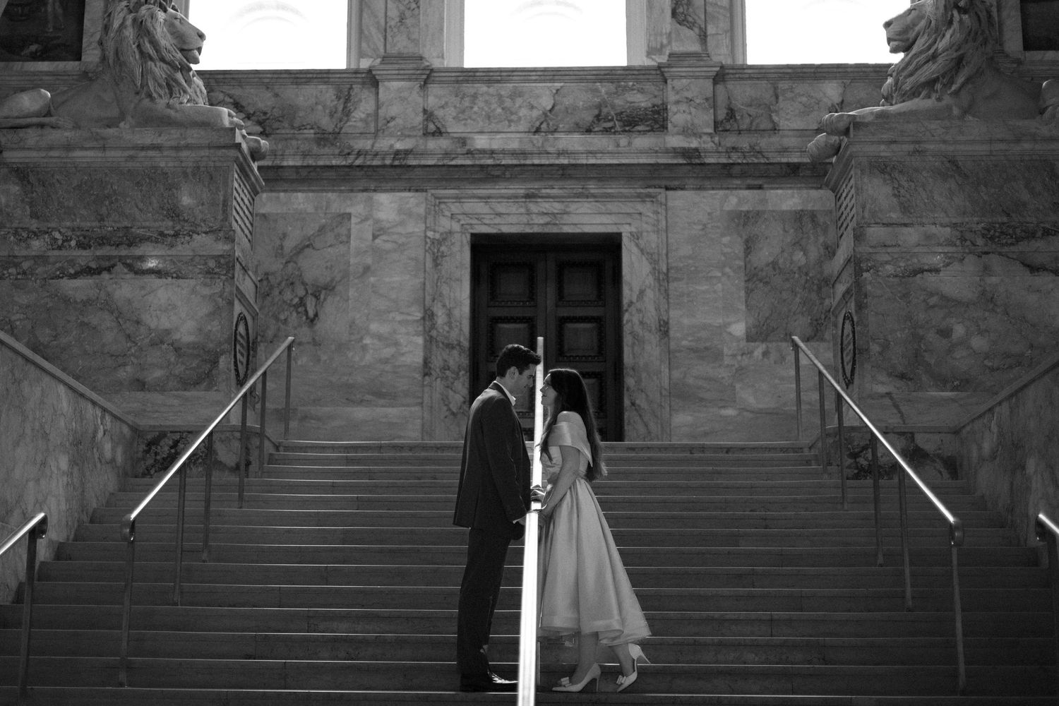 Four black and white photos show architectural details of a grand staircase with stone sculptures and decorative elements.