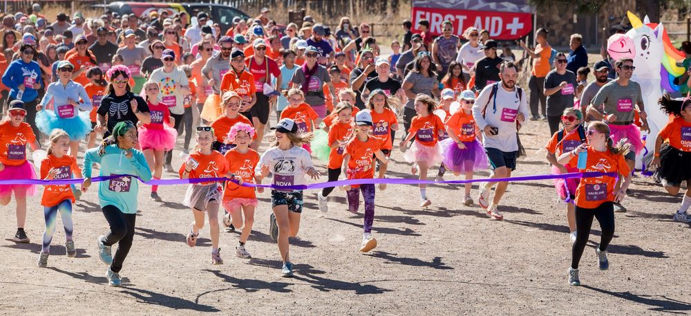 A large crowd of runners wearing orange shirts participate in a community race event on a sunny day.