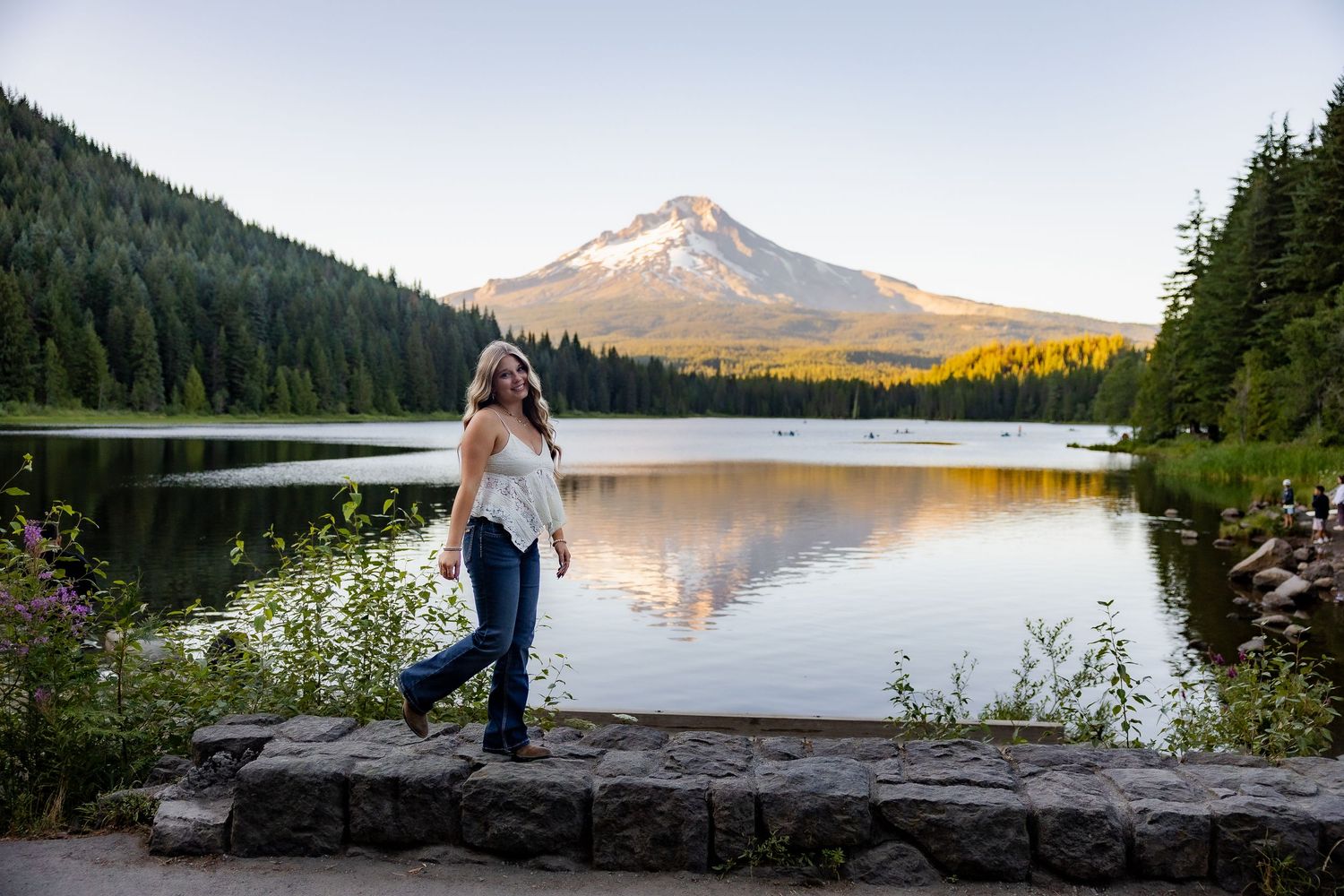 Panoramic view of mountain lake with wooden dock and evergreen forest at sunset.