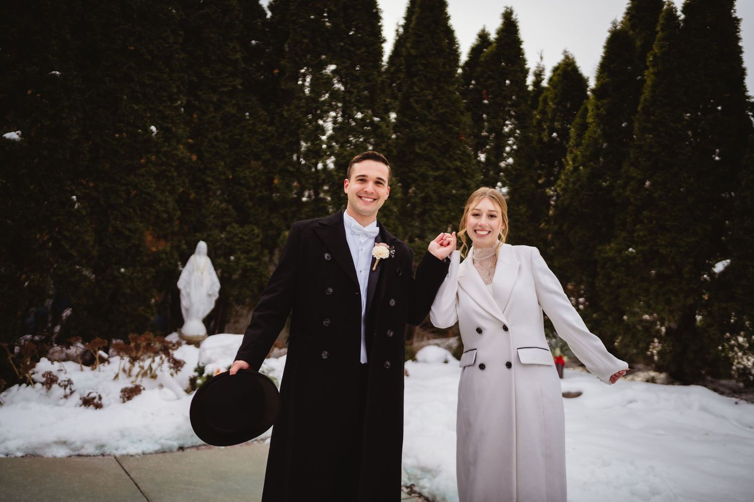 A couple poses together in a snowy winter landscape with evergreen trees in the background.