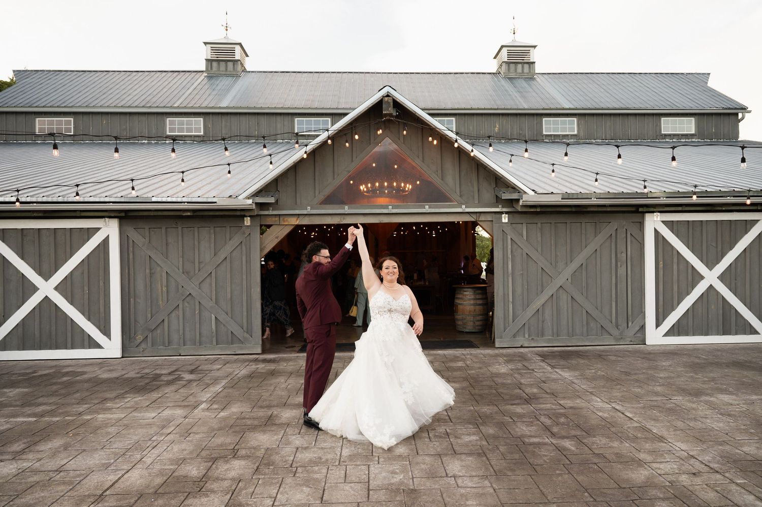 Wedding ceremony takes place under a rustic wooden pavilion with exposed beams and scenic view through archway in background.