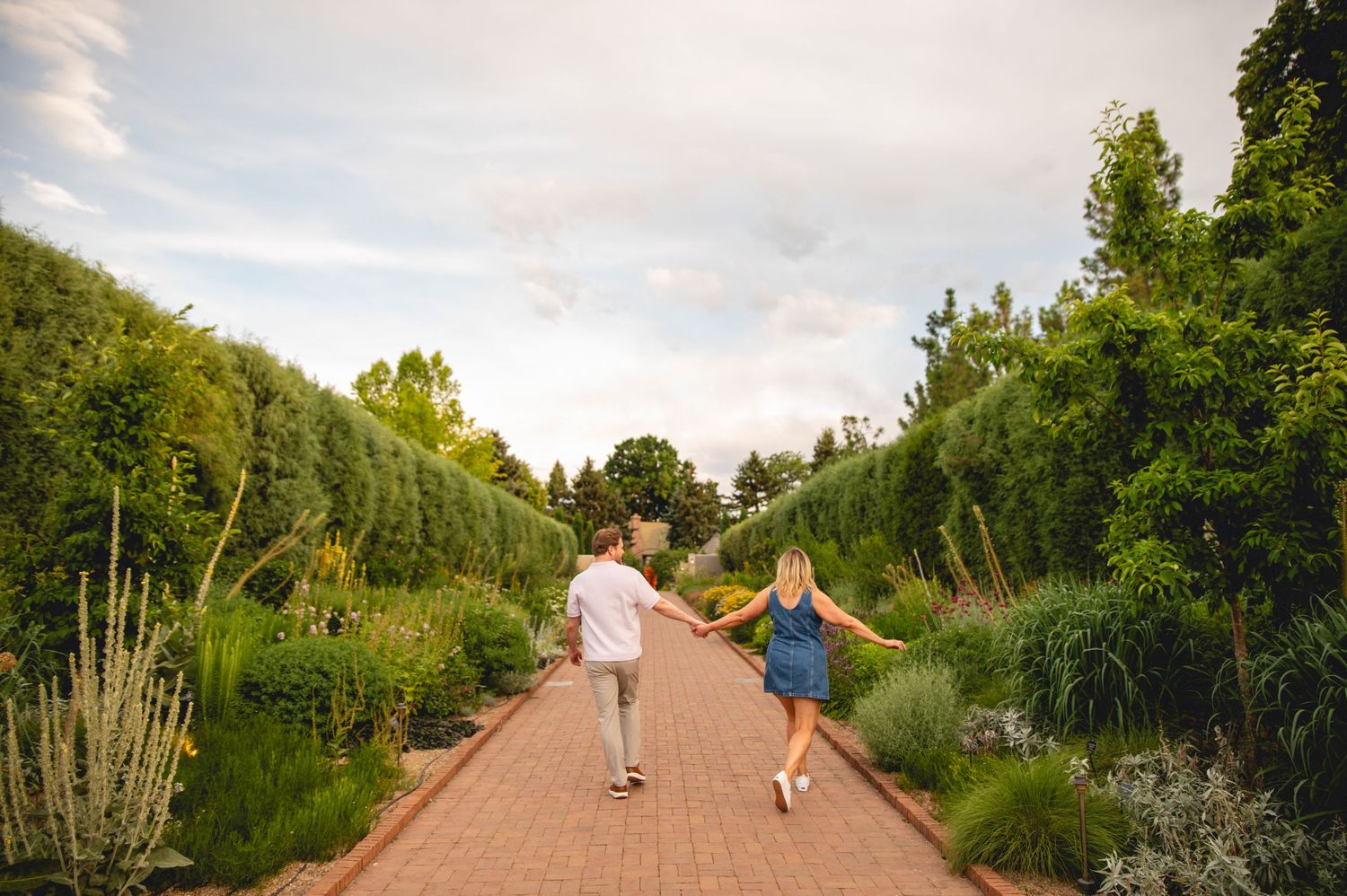 People walking and jogging on a scenic trail surrounded by lush green trees and vegetation on a sunny day.