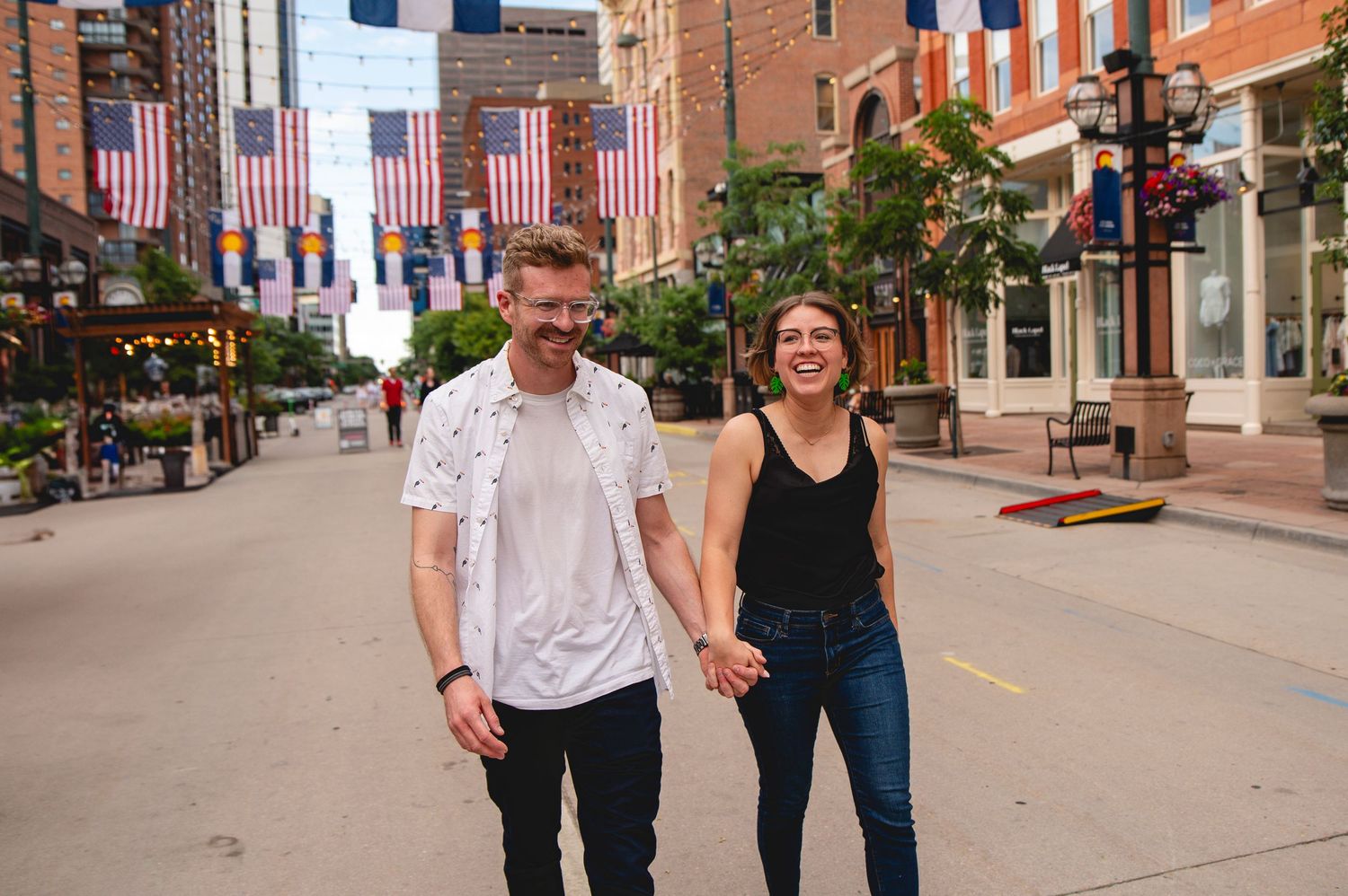 Couple walking hand in hand down a brick sidewalk with American flags displayed on storefronts.