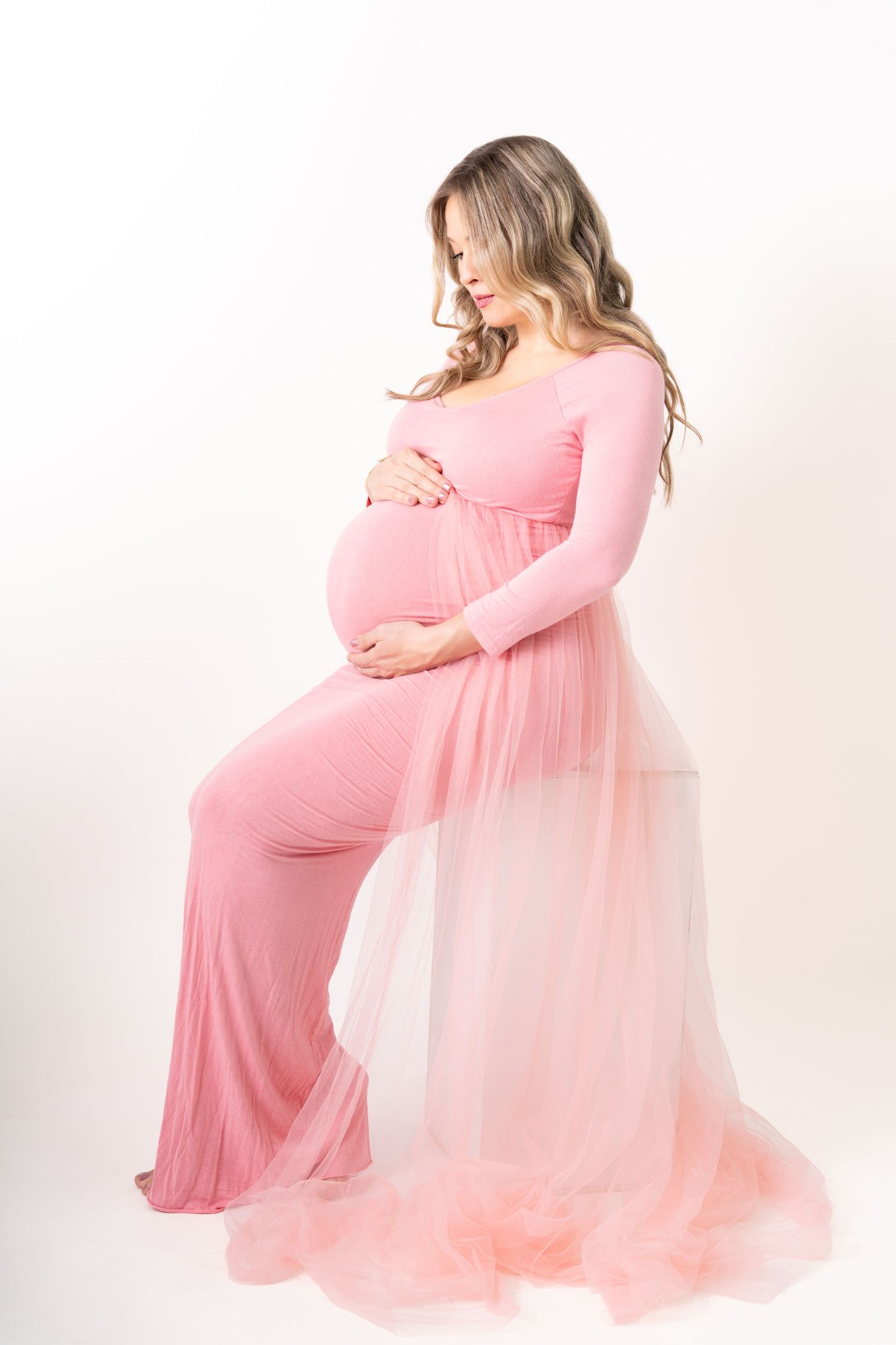 Ethereal maternity photo with flowy light blue gown and floral arch featuring blue blossoms against grey backdrop.