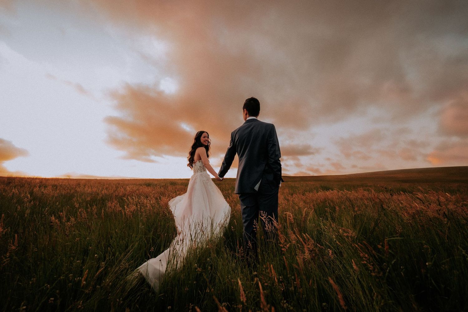 Silhouetted newlyweds walking through golden field at sunset.