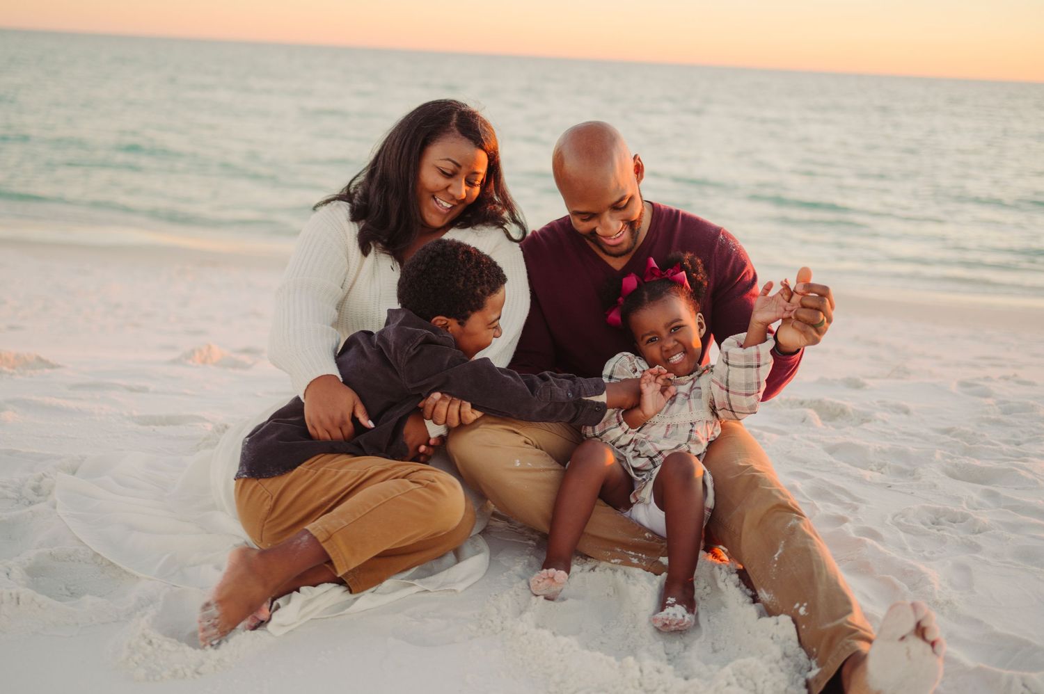 A family enjoys a playful moment together while sitting on the beach at sunset.