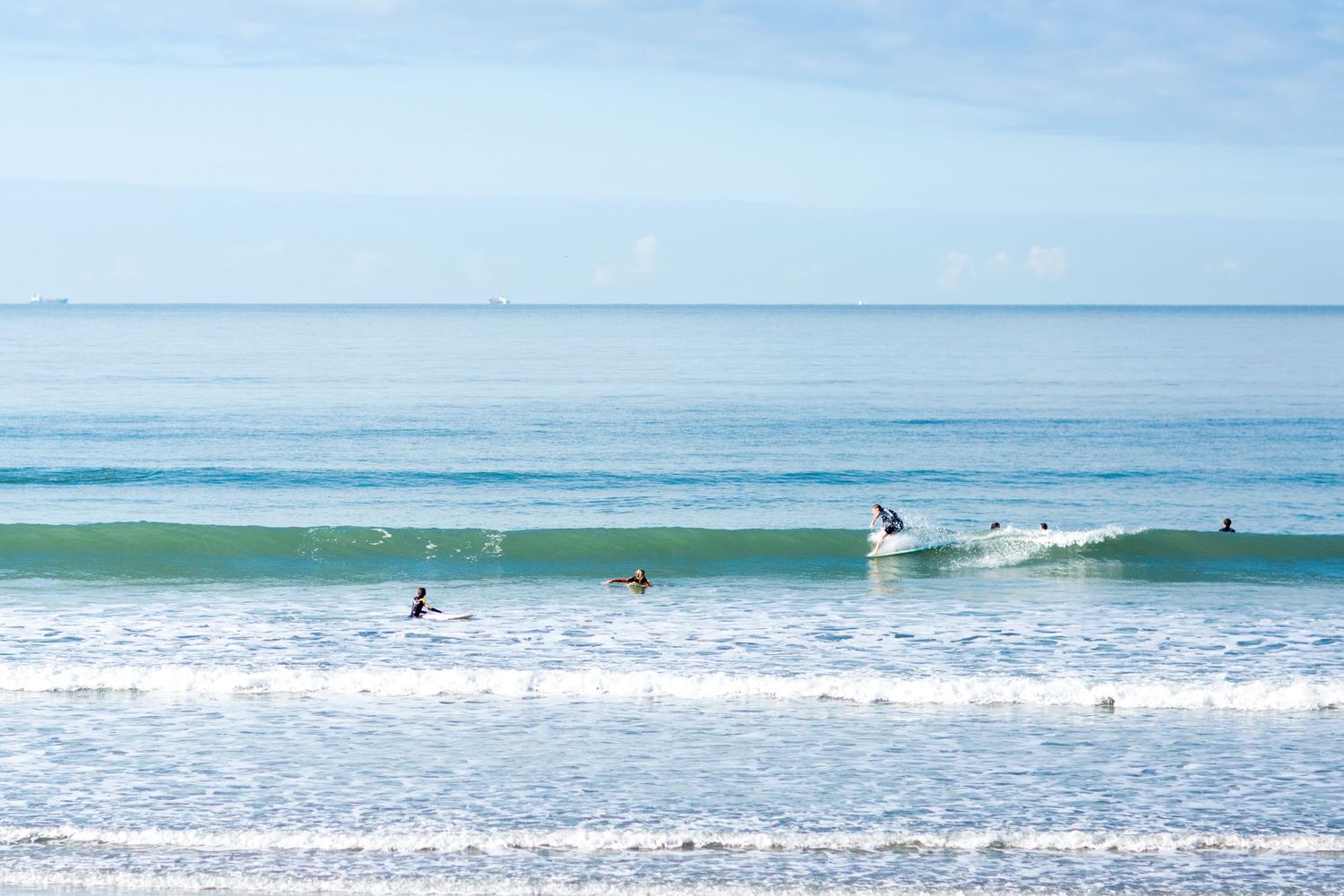 Surfers catching waves on a beautiful turquoise ocean under a bright blue sky.