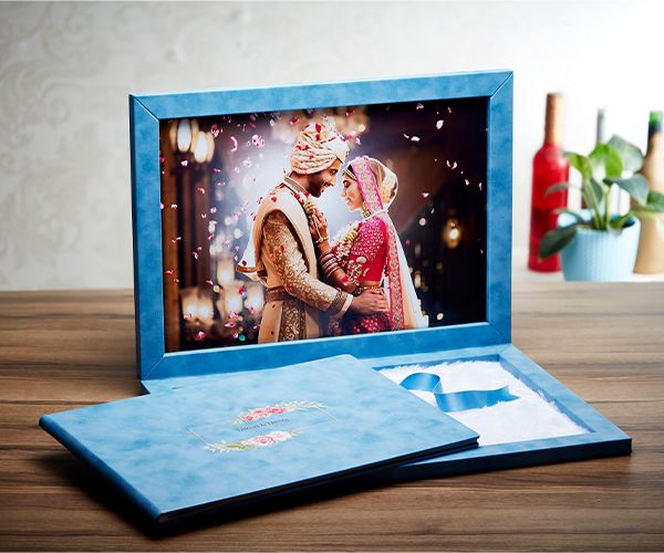 A blue photo frame displaying a wedding photo sits on a wooden surface with decorative bottles in the background.