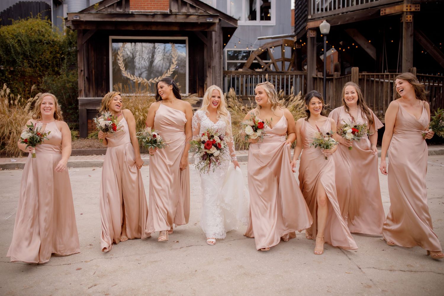 Bridesmaids in blush pink dresses pose with bride on wedding day outdoors.