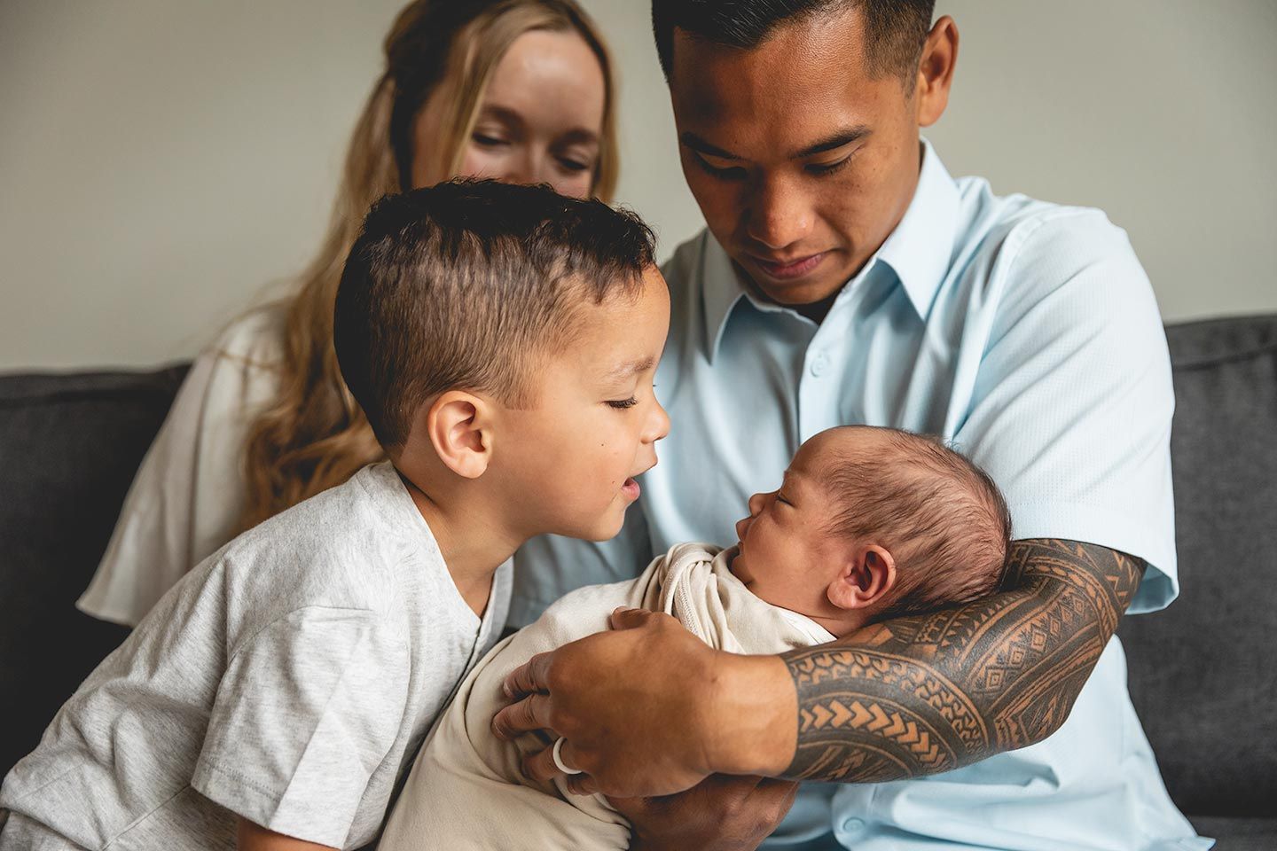 father holding newborn baby while toddler brother looks into eyes
