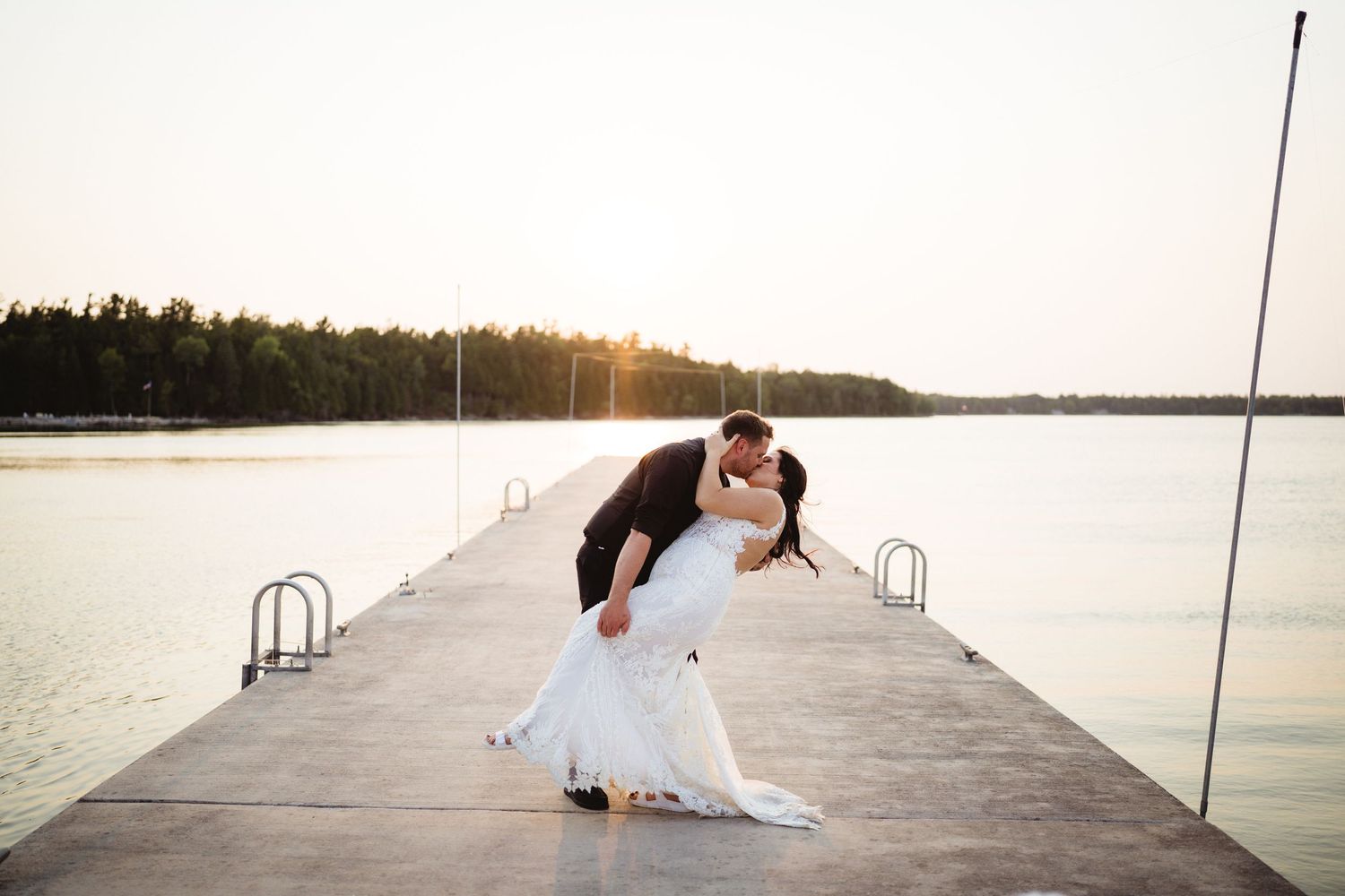 Romantic dip pose on wooden pier at sunset overlooking calm waters.