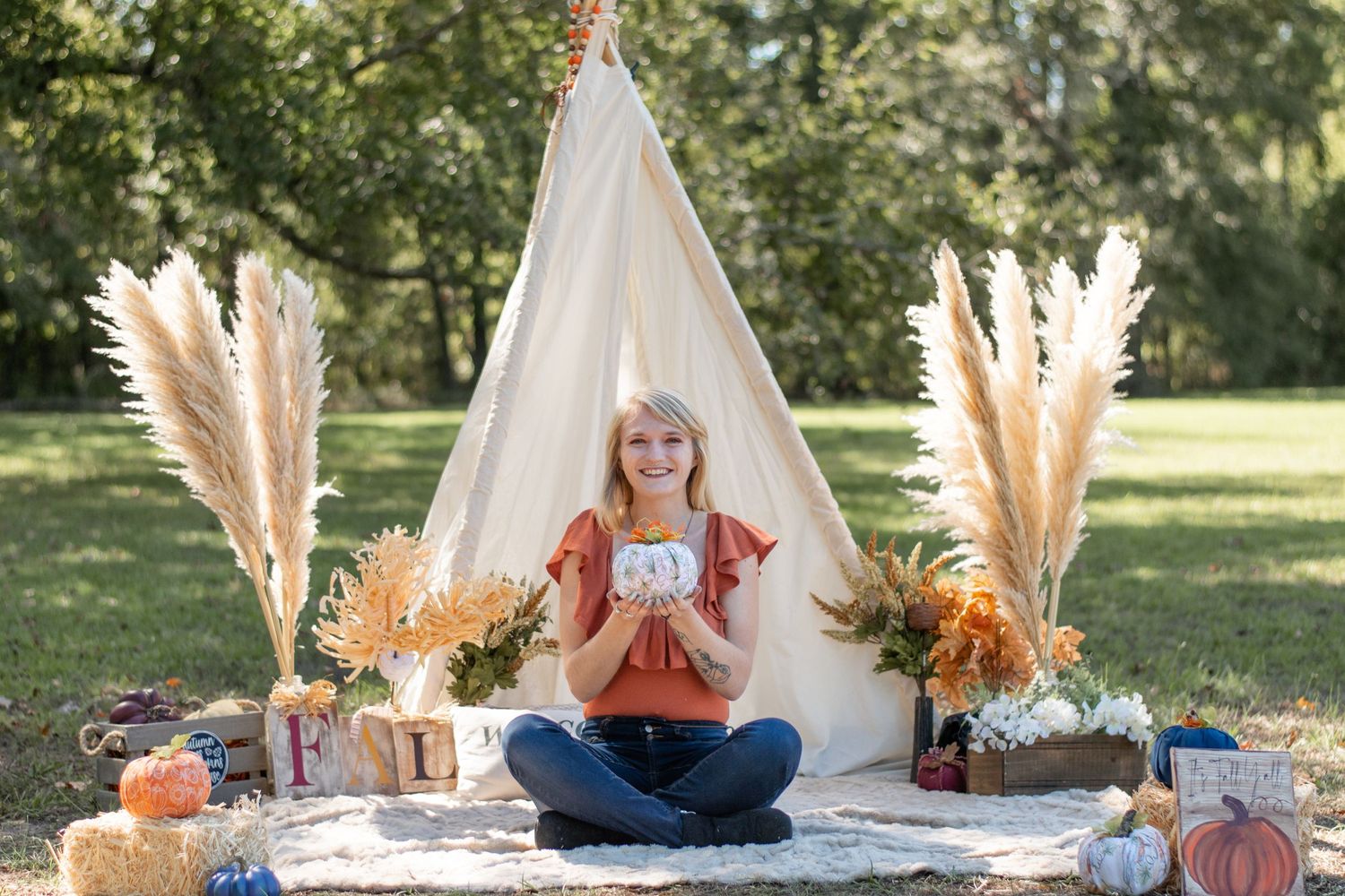 Boho outdoor setup with person sitting cross-legged in front of white teepee with pampas grass decor.