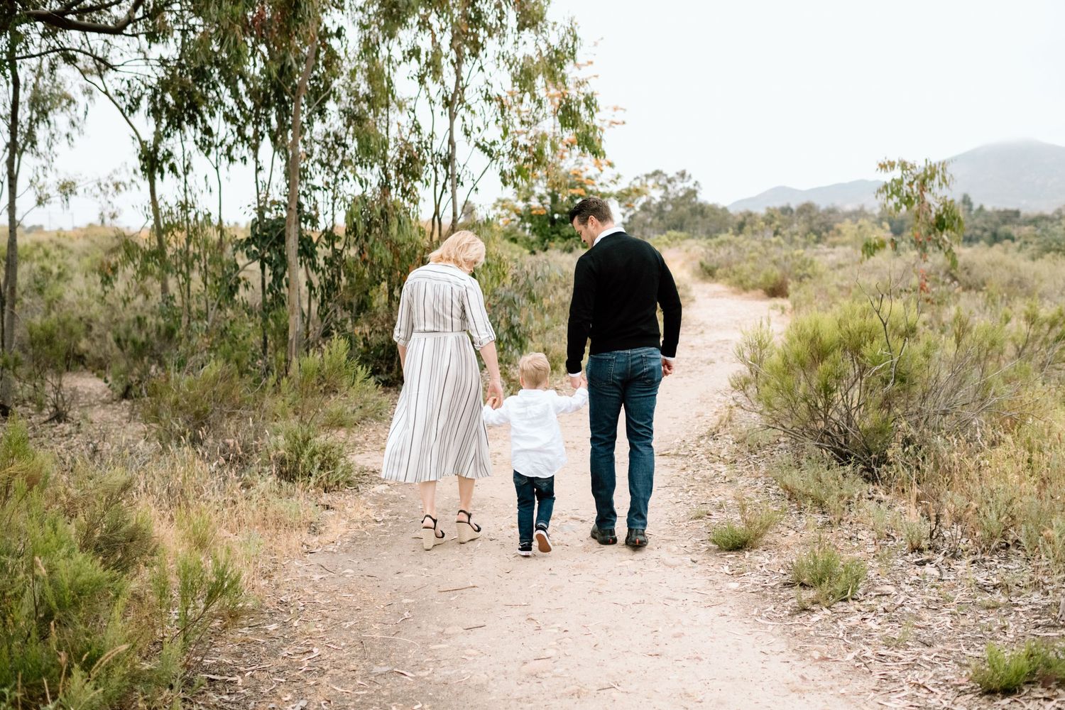 Family walking together on desert trail with eucalyptus trees in background.