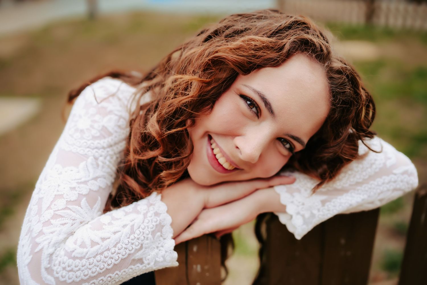 Cozy winter portrait wearing white knit sweater leaning on wooden railing.