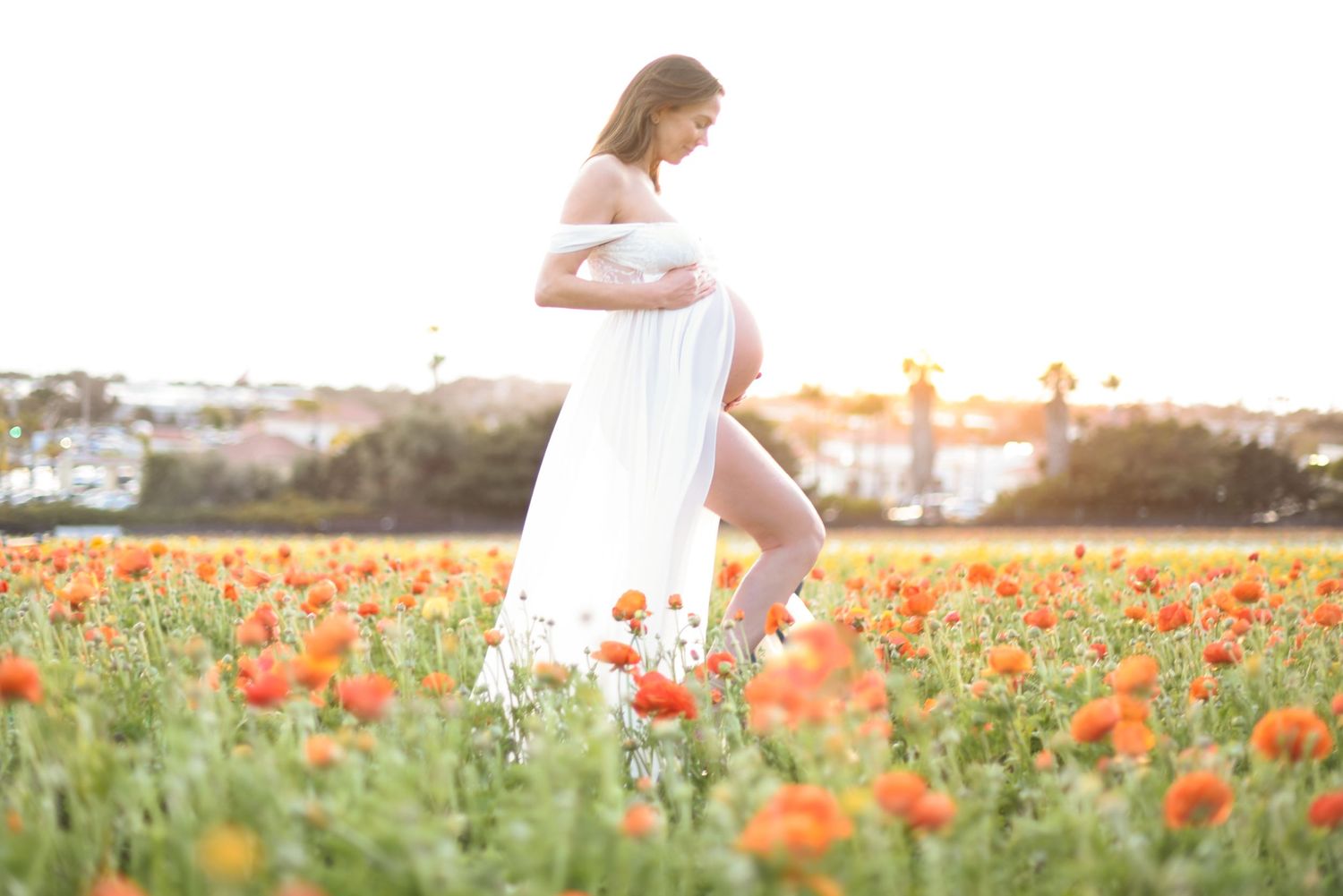Woman in white dress walks through vibrant orange poppy field during golden sunset.