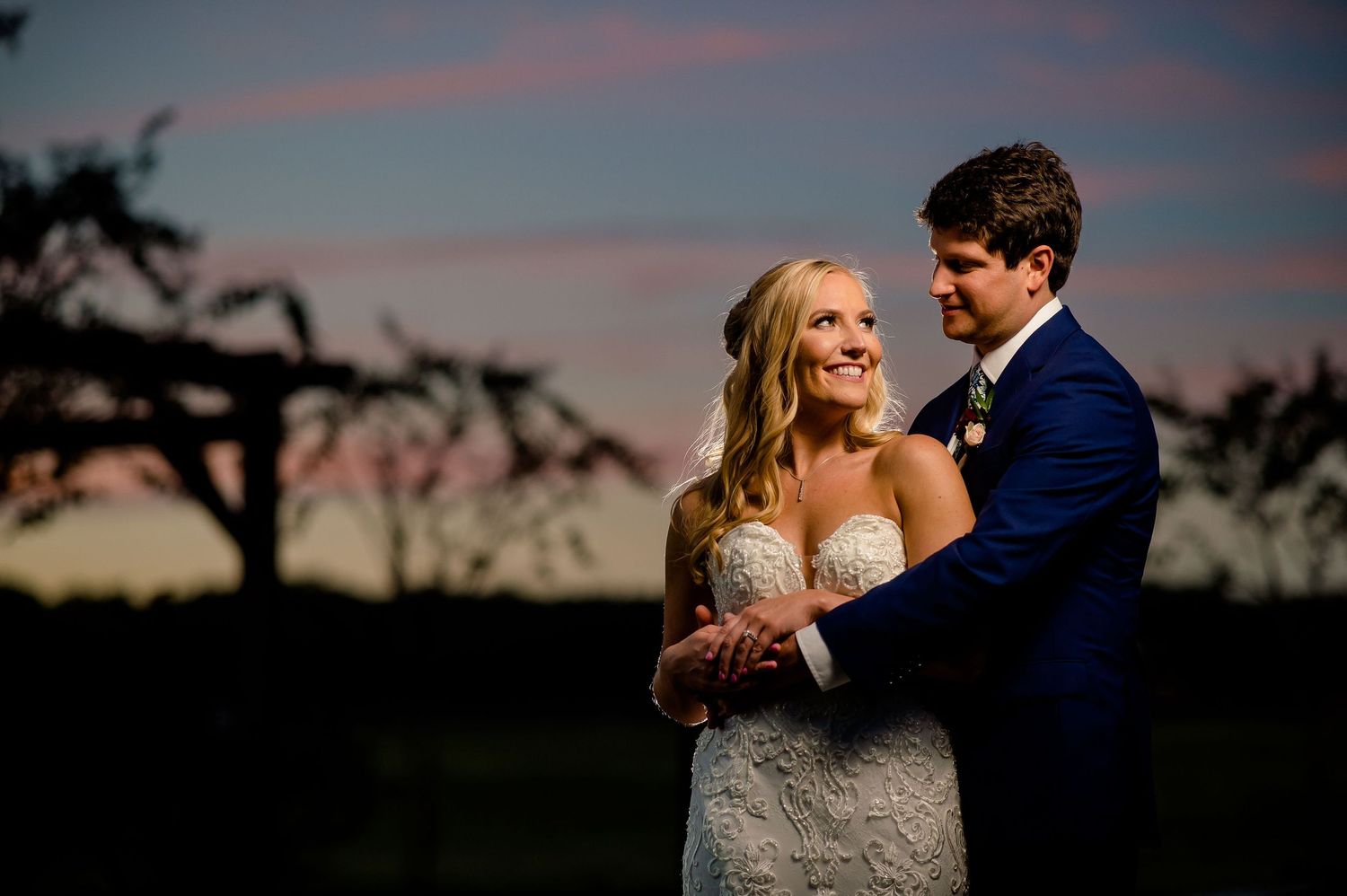 Romantic sunset portrait of newlyweds embracing in front of dusky sky.