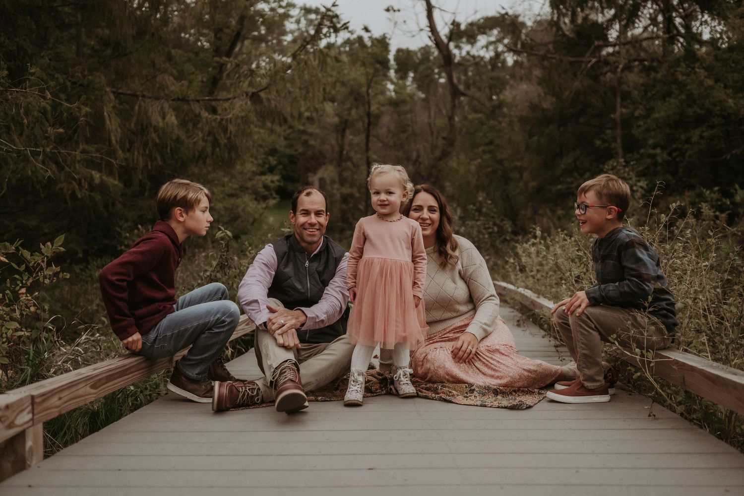 A family sits together on a wooden boardwalk during a sunset photo session.