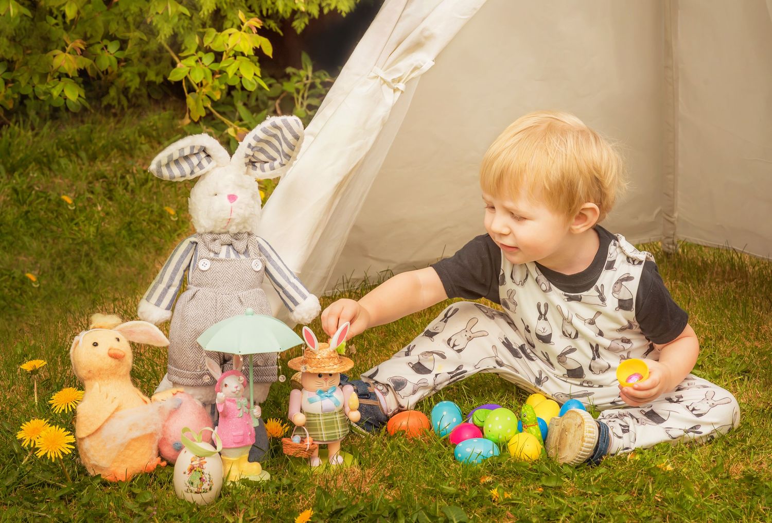 Outdoor scene with plush toys and colorful Easter eggs arranged on grass near a tent.
