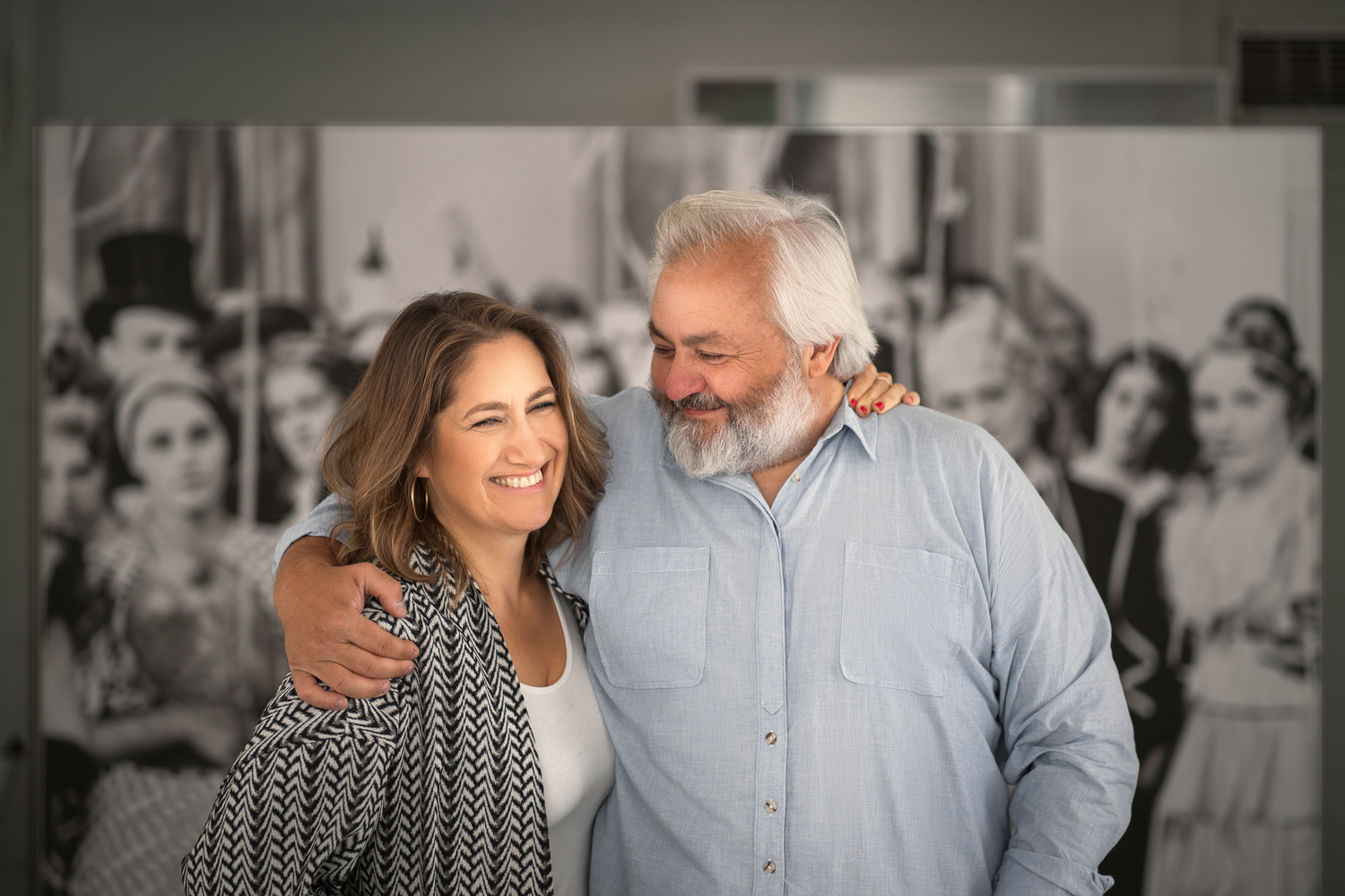 A couple shares a warm embrace while smiling at an indoor gathering.