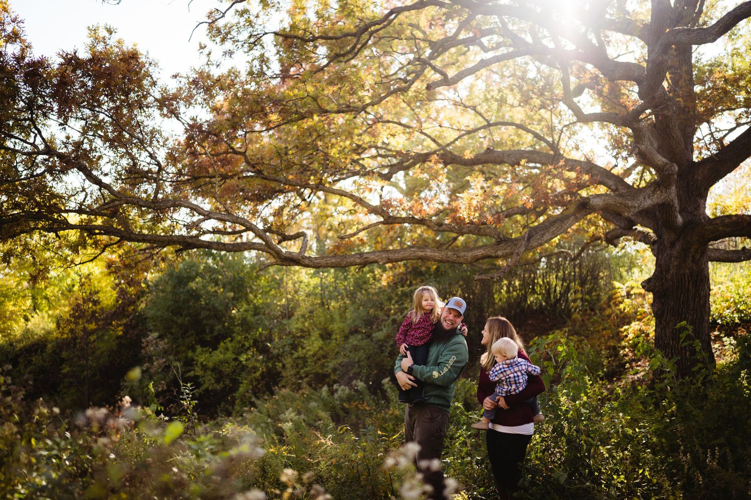 Family walking together through sunlit autumn trees during golden hour.