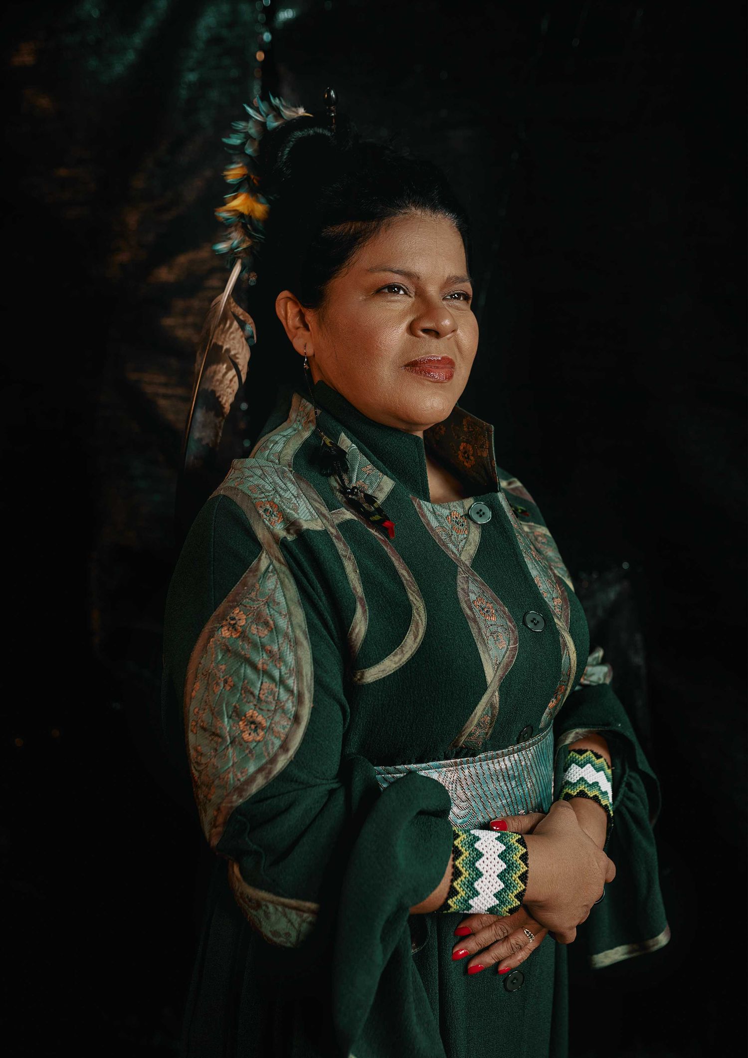 Portrait in traditional Native American regalia featuring intricate green and silver patterns.