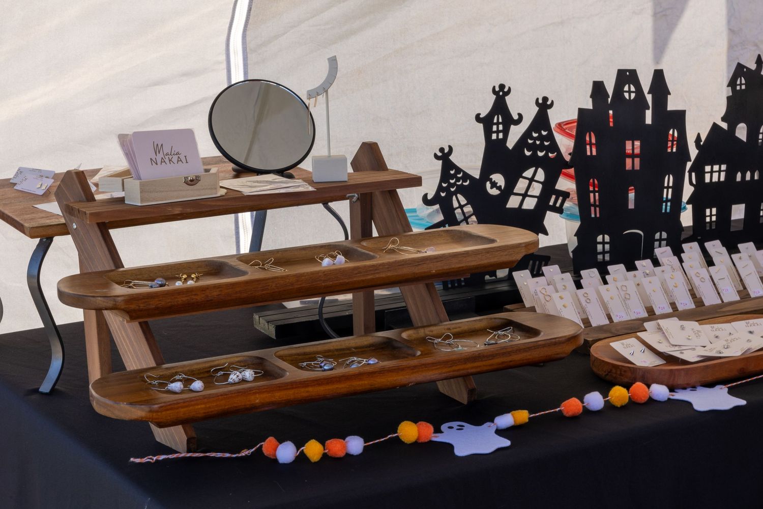 Wooden tiered jewelry display stand with Halloween haunted house decorations at a craft fair.