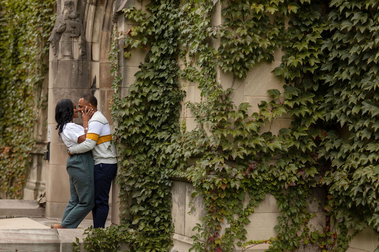 A romantic couple embraces against an ivy-covered stone wall creating an intimate outdoor moment.