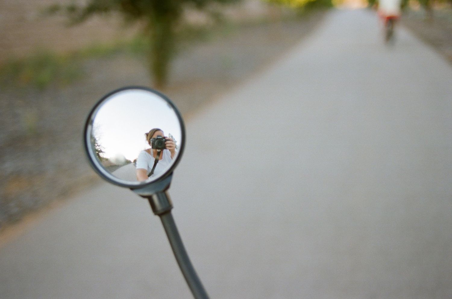 Bike mirror reflection showing a blurred path and distant figure.