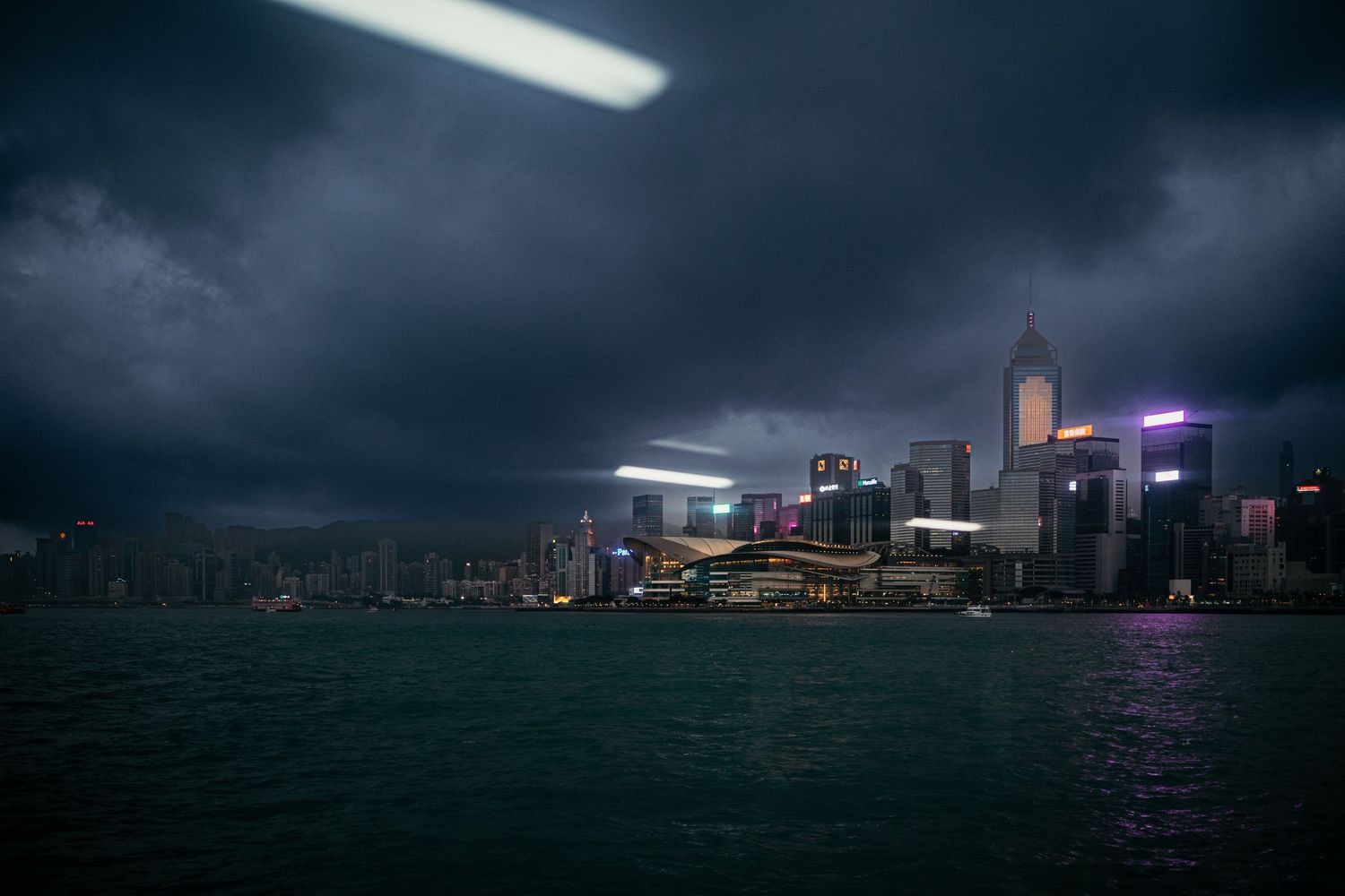 Dramatic cityscape of Hong Kong's illuminated skyline at night during a storm.
