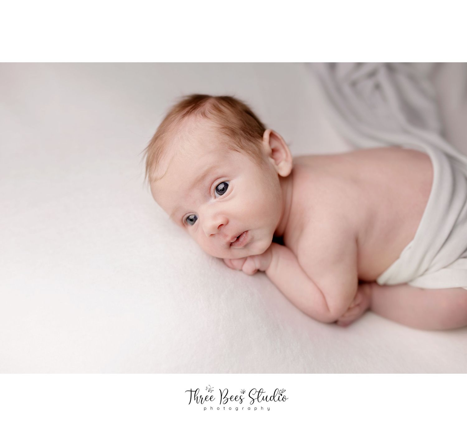 Newborn baby lying on white fabric in gentle lighting during professional photo session.