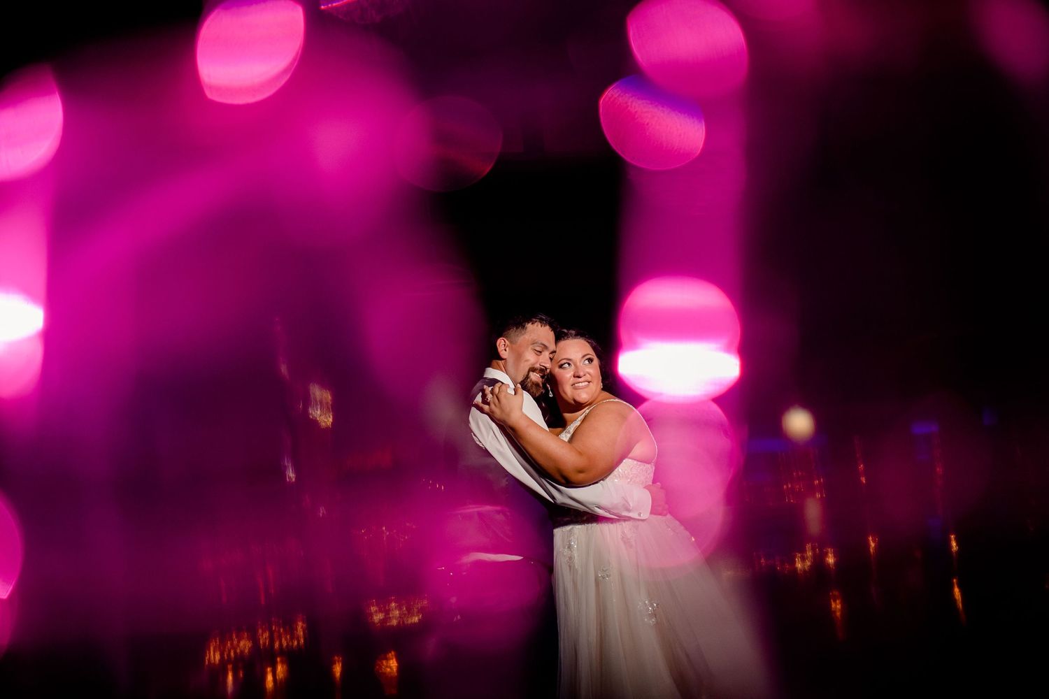 Romantic dance moment with pink lighting and bokeh effects at wedding reception.