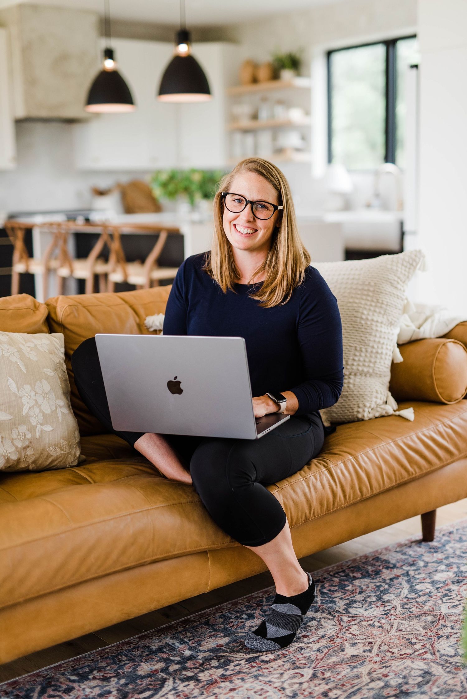 photo of carolyn of stonewheel photography comfortably seated on couch in picturesque home with open laptop on lap smiling looking at camera
