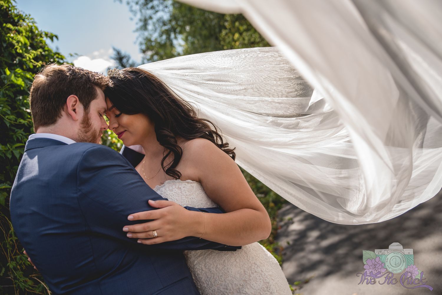 A flowing white wedding veil blows dramatically in the wind during an intimate couple's portrait.