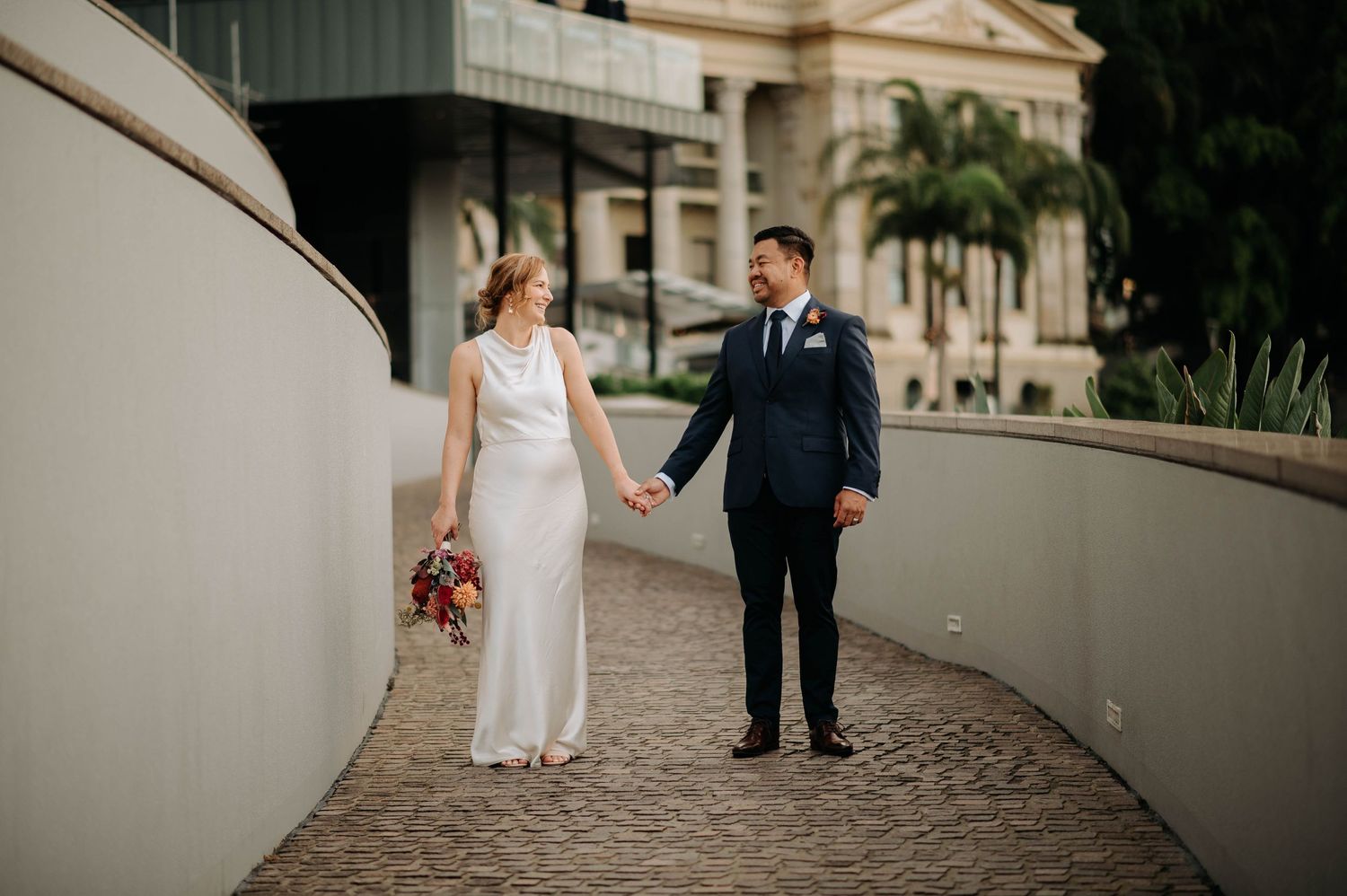 A bride and groom share a moment while walking along a curved pathway.