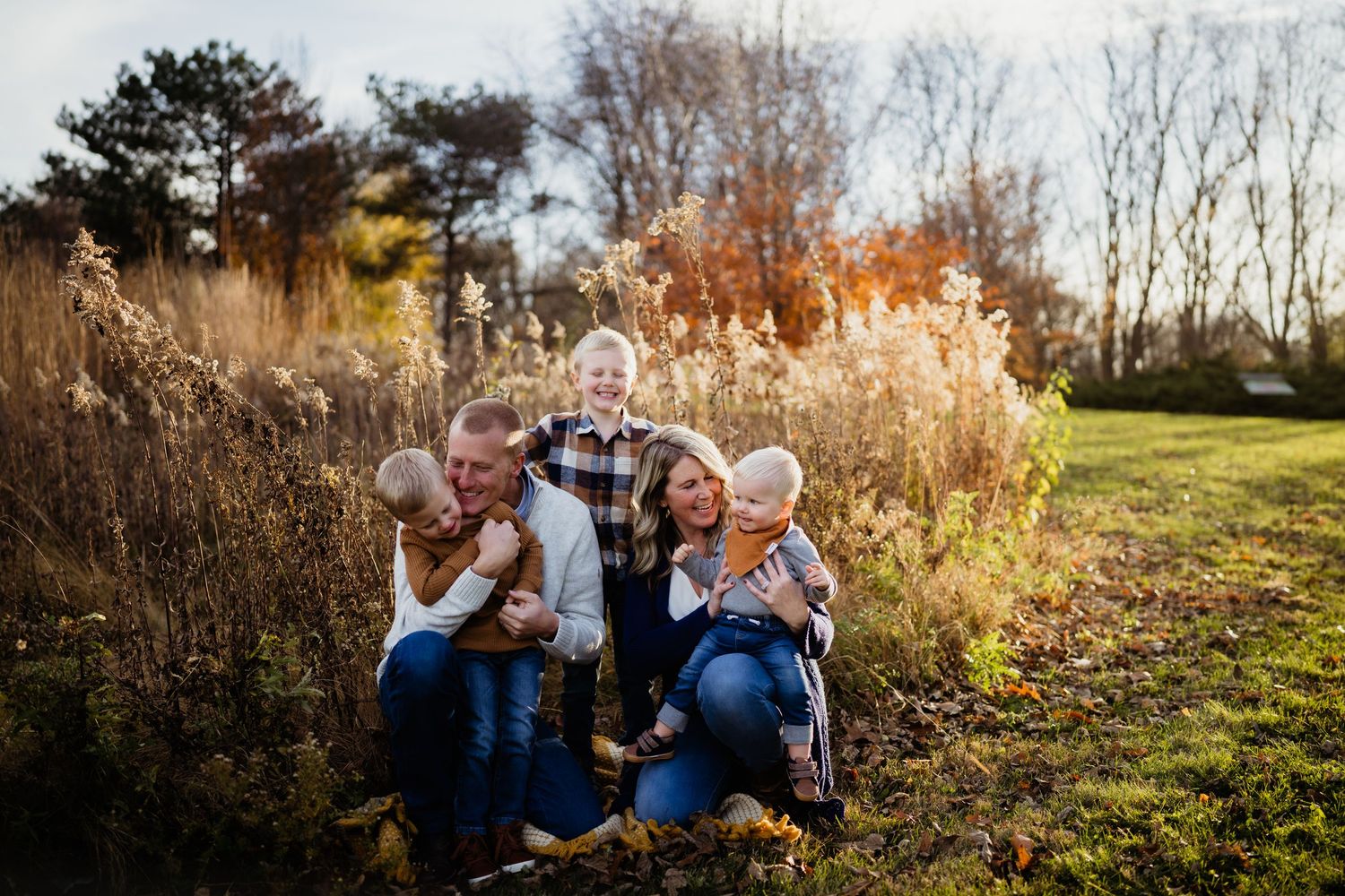 A family group poses together outdoors in a field of tall grass during golden hour.