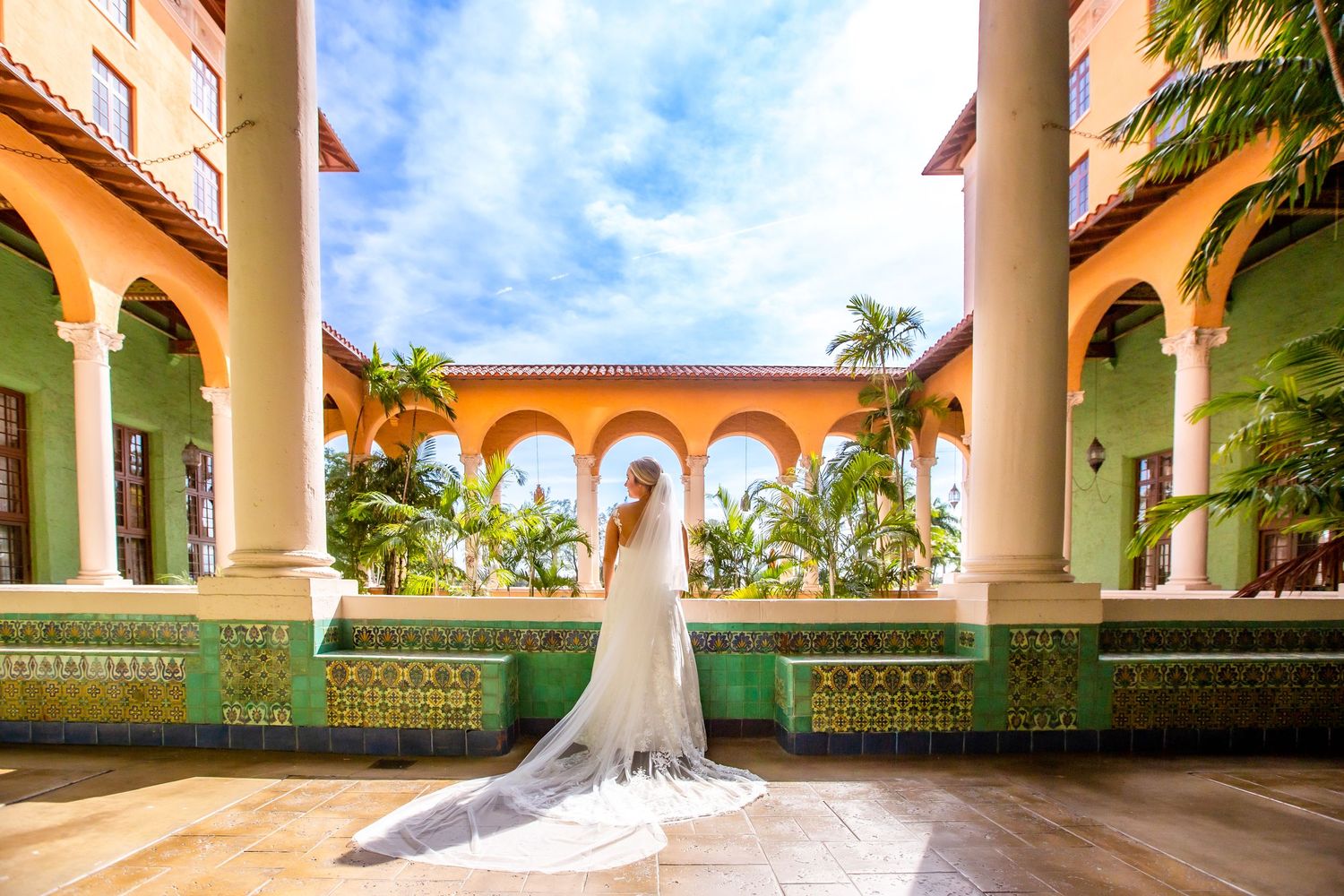 Mediterranean style courtyard with arched columns and palm trees under blue sky.