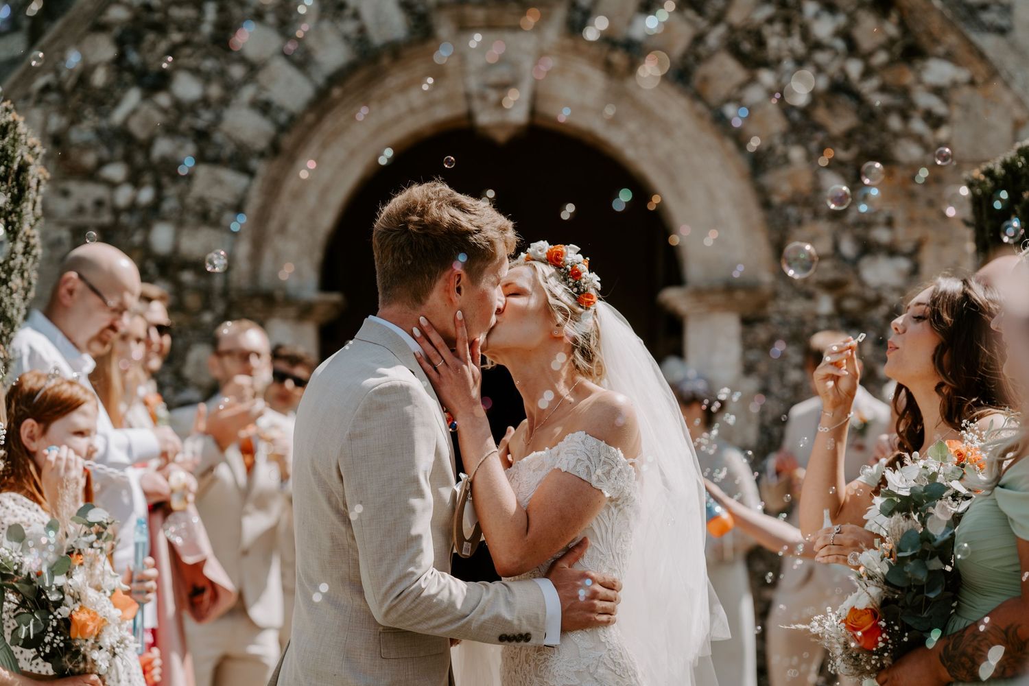 Bride and groom kissing while guest blow bubbles around them instead of throwing confetti.