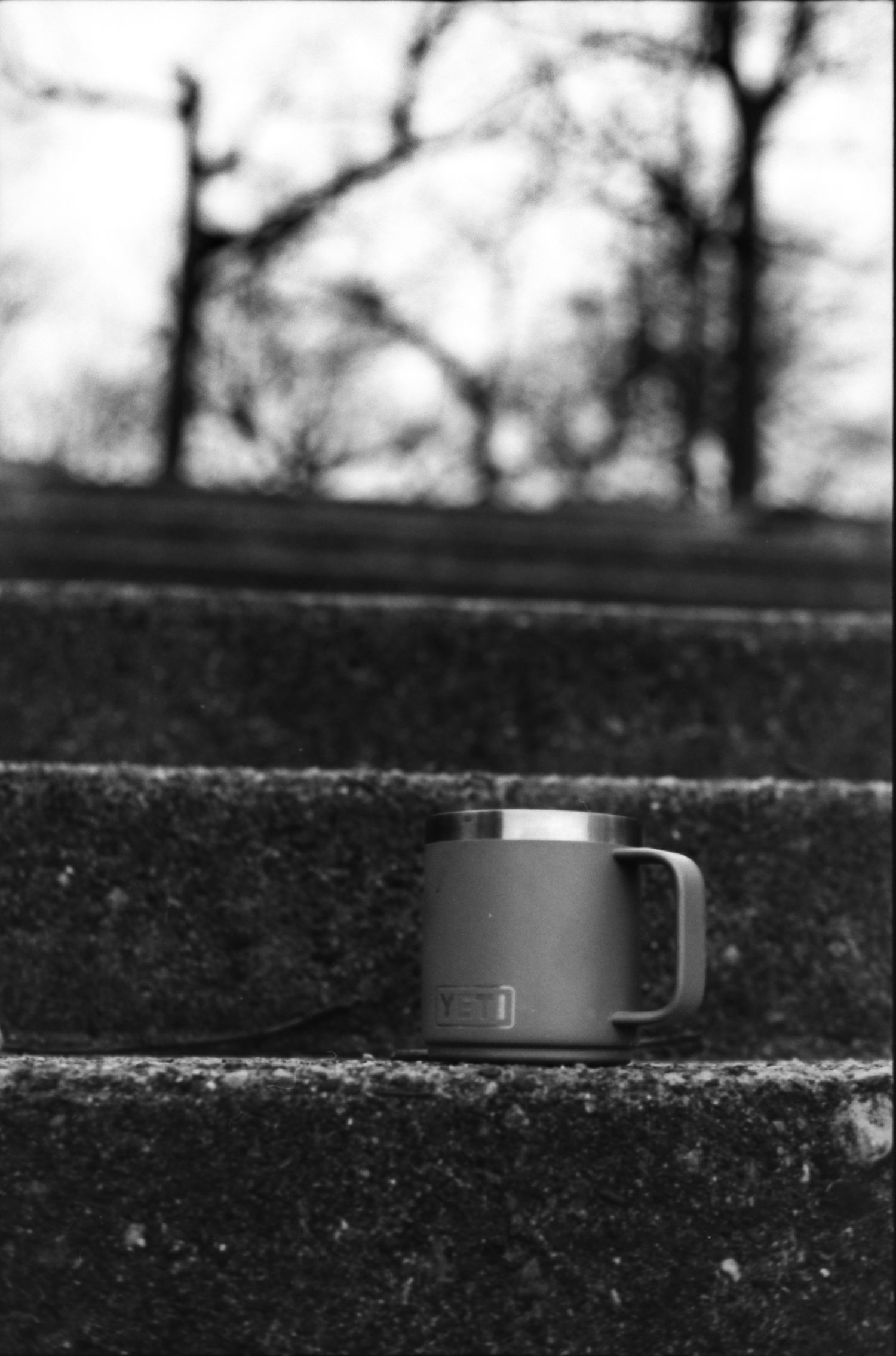 Metallic travel mug sitting alone on concrete steps in moody black and white.