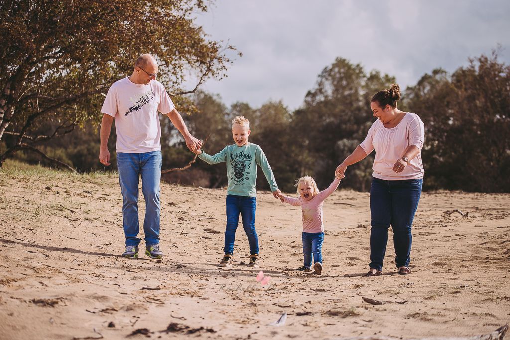 Family of four holding hands while walking on a sandy beach path.