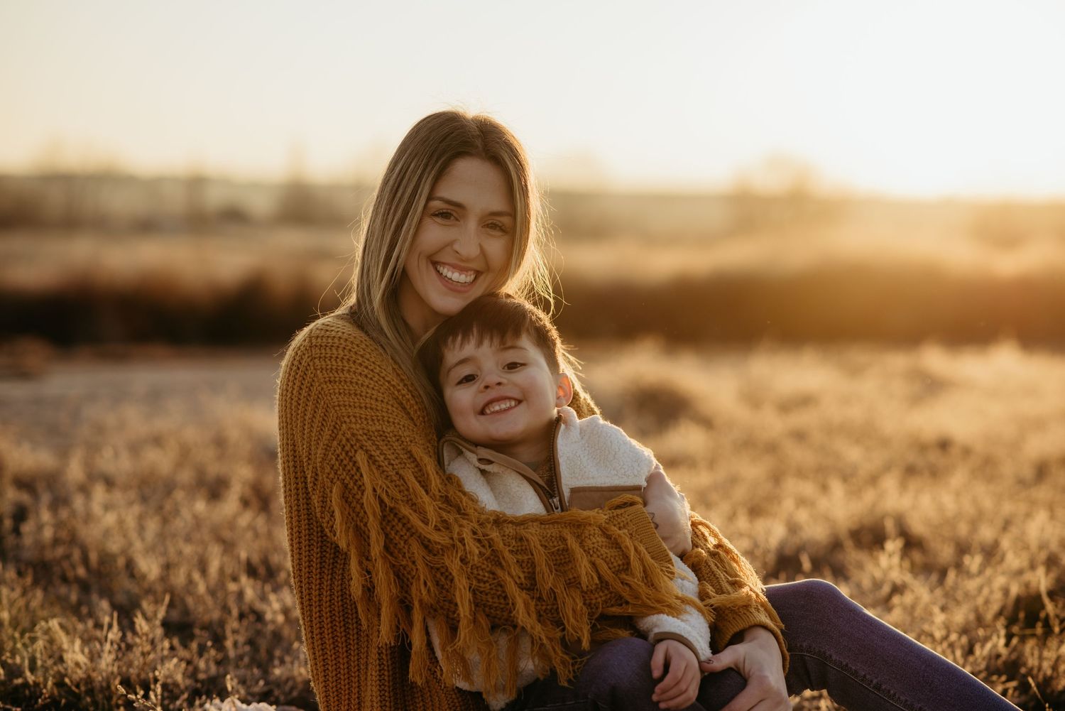 lifestyle family photos of a mom holding her son in a field at sunset