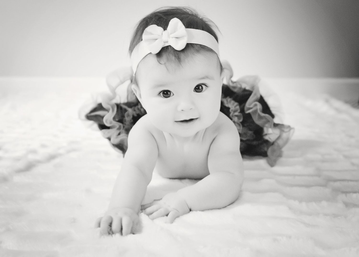 Black and white portrait of baby wearing bow headband on white backdrop.