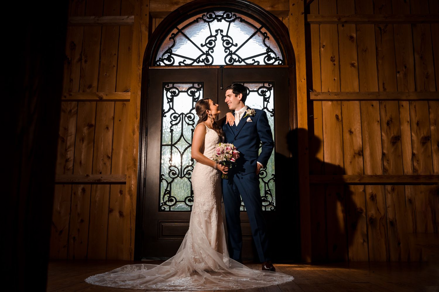 Couple poses in rustic wooden chapel with ornate arched windows.